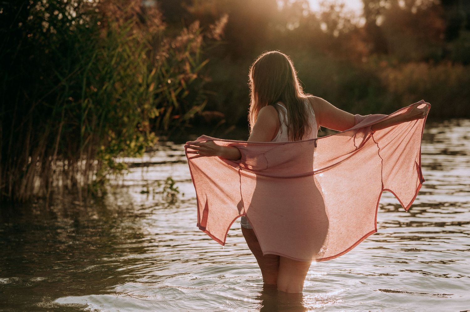 Sinnliches Boudoir-Shooting im Wasser bei Sonnenuntergang: Frau mit Tuch im Gegenlicht, feminin, frei und kraftvoll.