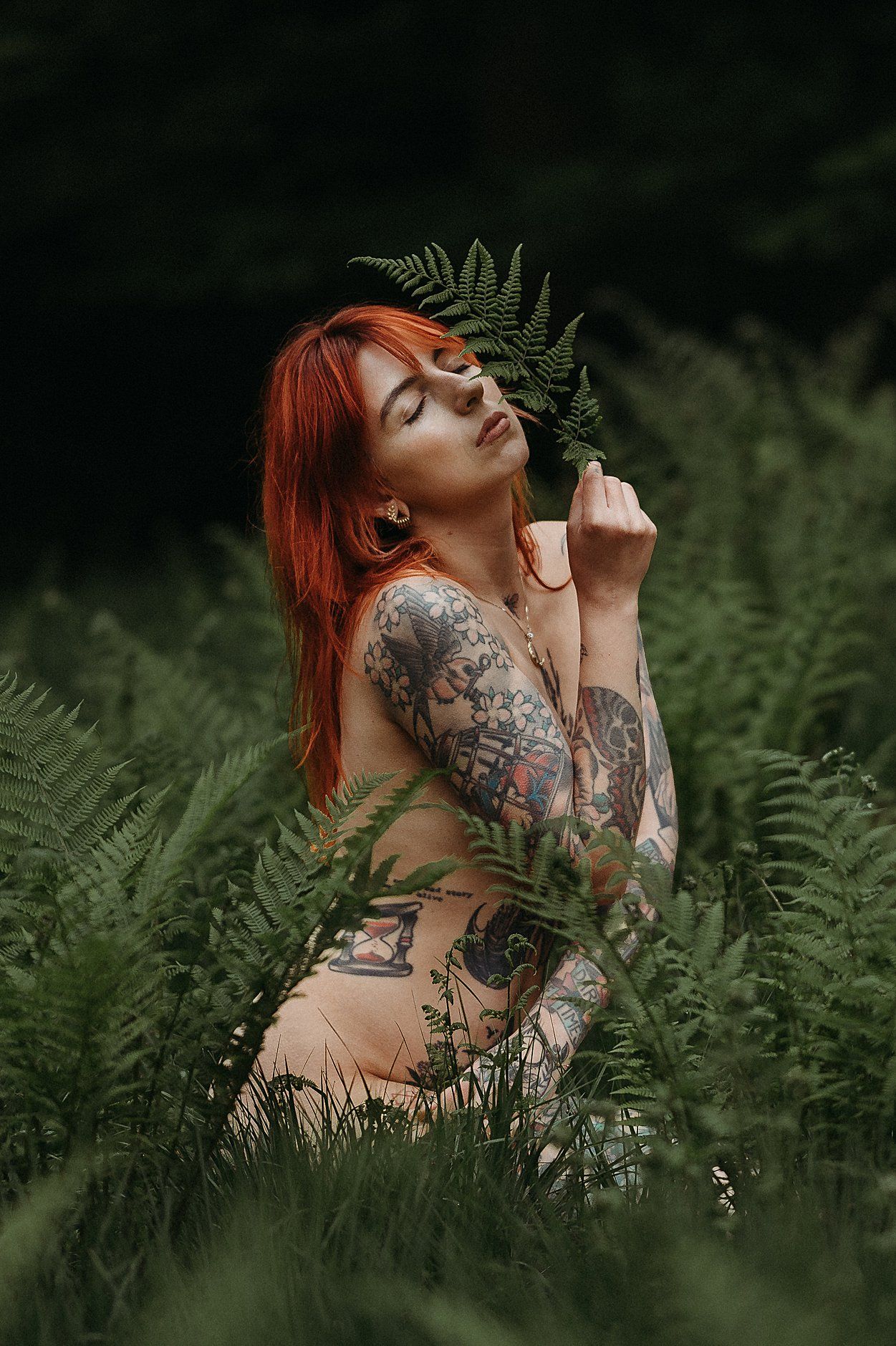 Frau mit rotem Haar und Tattoos sitzt in hohem Farm bei einem Boudoirshooting im Wald