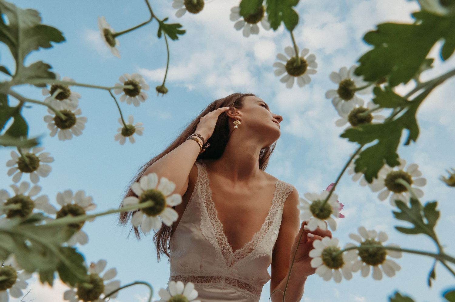 Frau im Spitzenkleid zwischen Blumen vor blauem Himmel – verträumtes Sommer-Portrait in der Natur voller Leichtigkeit und Freiheit.