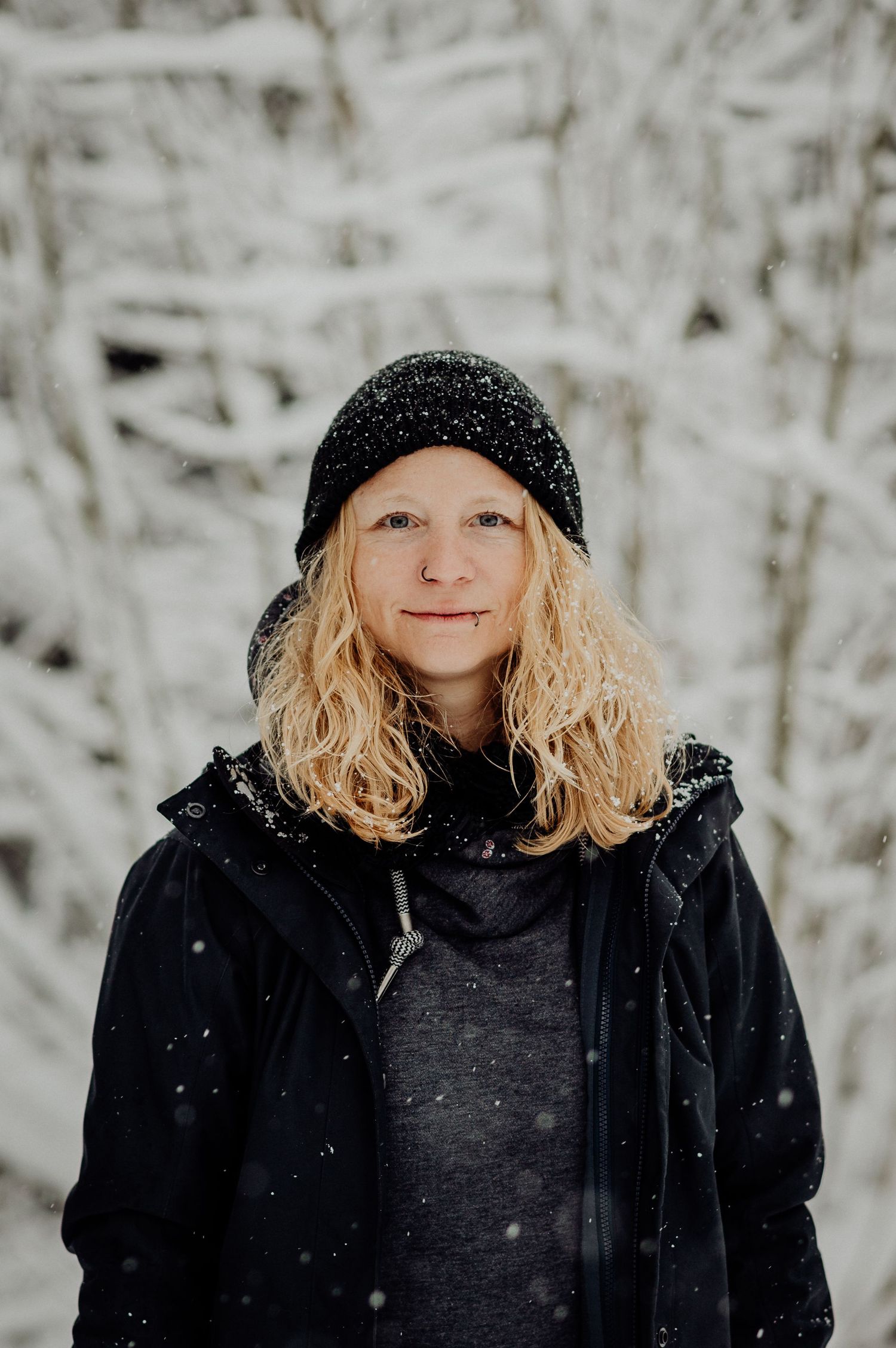 Frau mit Mütze im tief verschneiten Winterwald im Berner Oberland. Portraitshooting in der Natur mit Weitblick und Winterzauber.