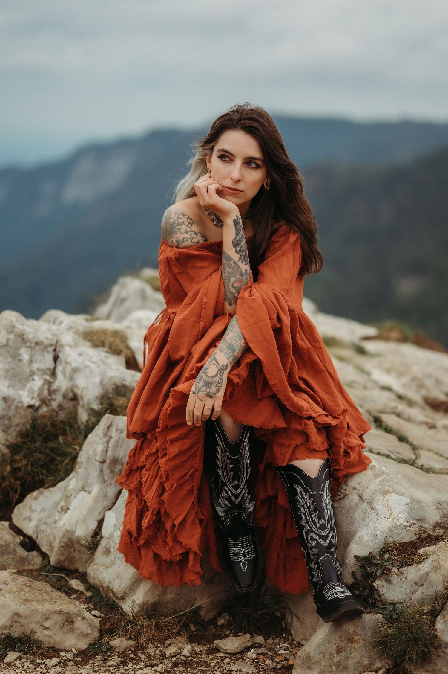 Frau in rotem Kleid am Creux du Van – kraftvolles Portrait vor dramatischer Felskulisse in der wilden Natur der Schweiz.