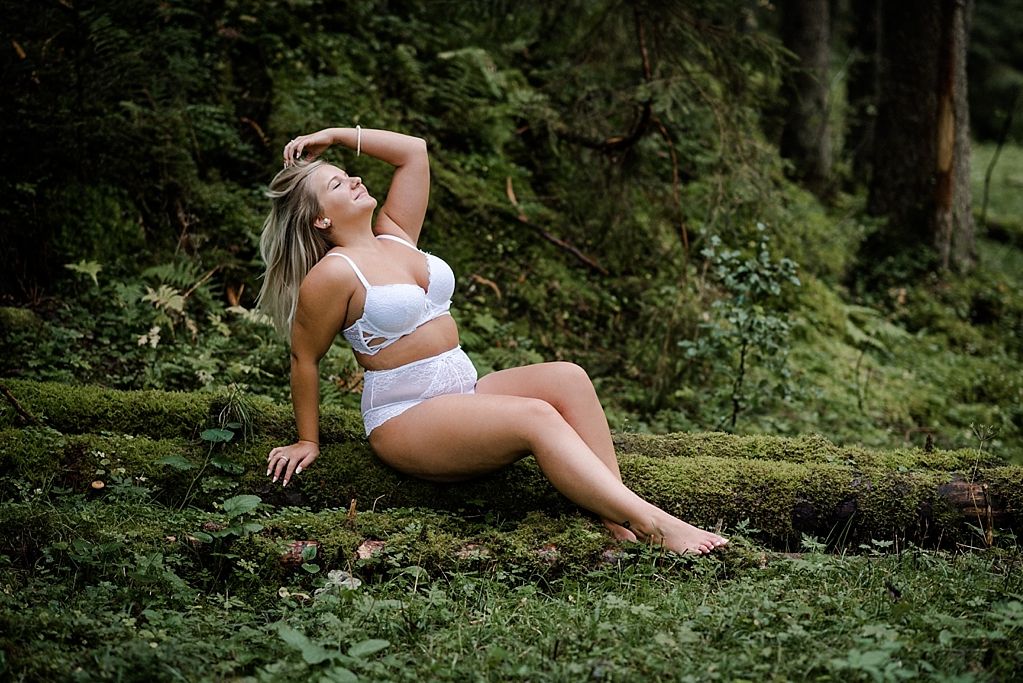 Frau in weisser Unterwäsche sitzt in einem Wald mit Moos bei einem Boudoirshooting in der Schweiz