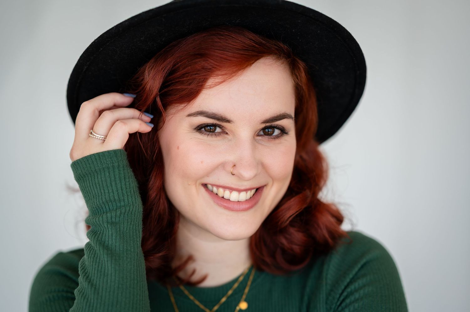 Junge Frau mit rotem Haar und schwarzem Hut lächelt selbstbewusst in die Kamera – Selbstliebe-Shooting mit Charme und Stil.