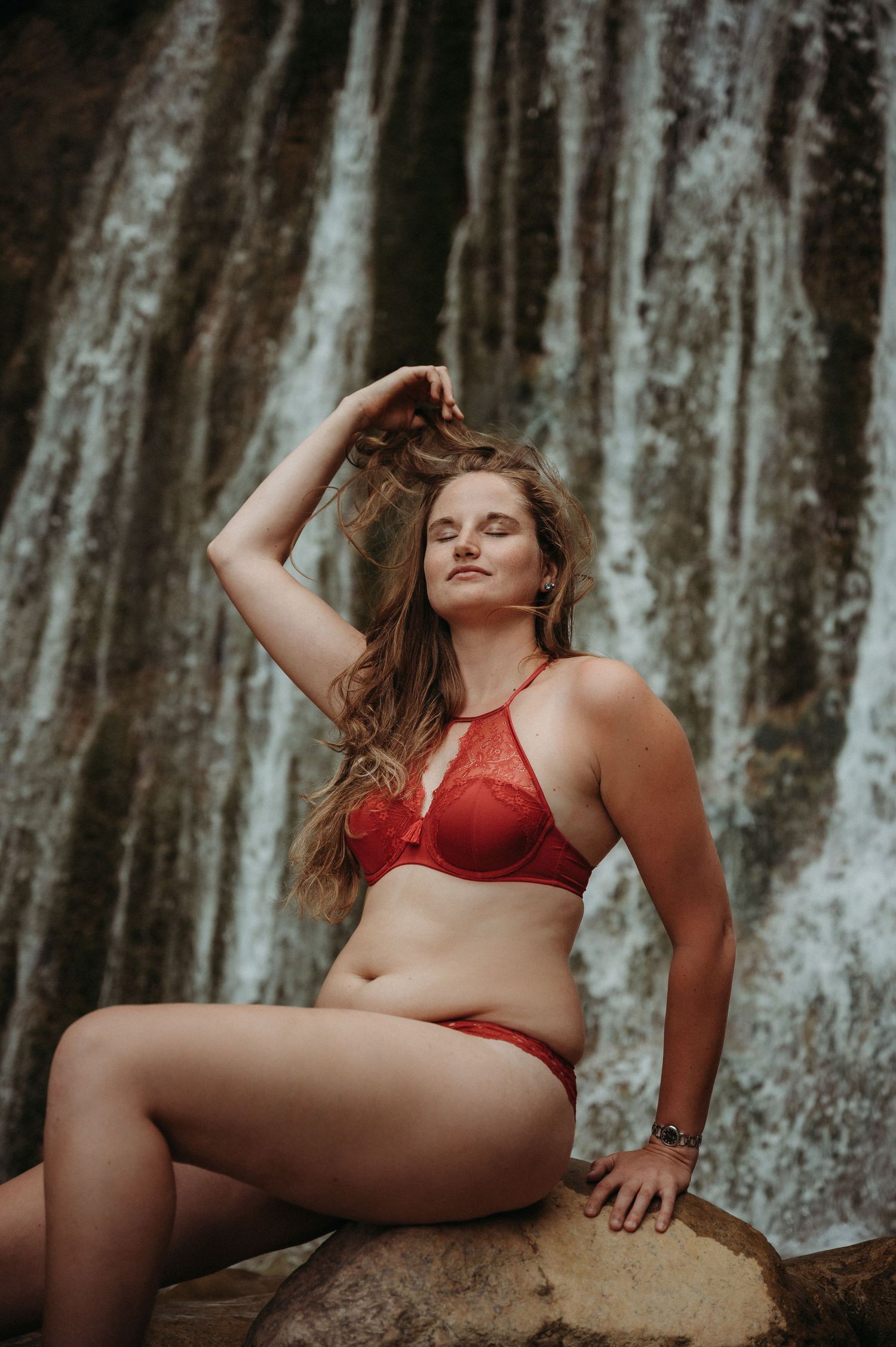 Selbstbewusste Frau in roter Lingerie sitzt vor Wasserfall bei Thun – Boudoirbild voller Sinnlichkeit, Stärke und natürlicher Schönheit.