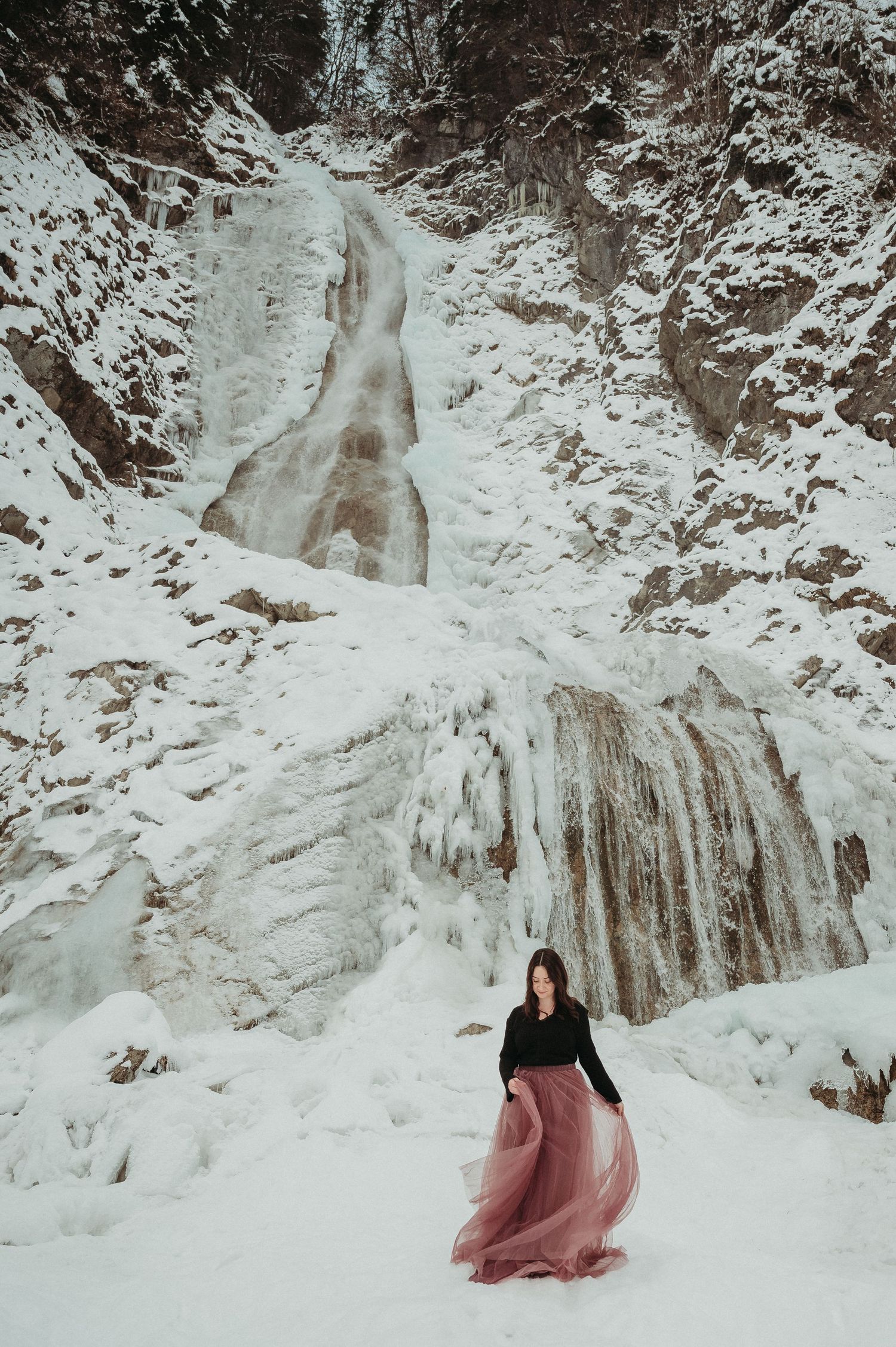 Frau im Tüllrock vor vereistem Wasserfall – märchenhaftes Wintershooting in beeindruckender Schneelandschaft.