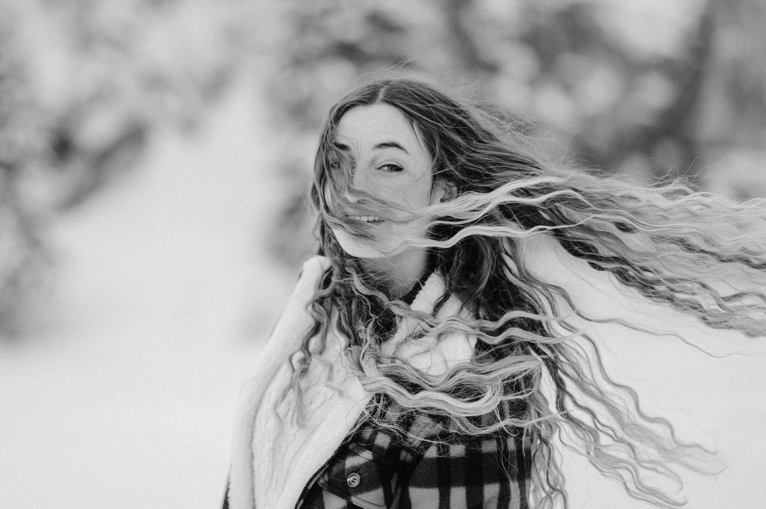 Porträt einer Frau mit wehenden Locken im Schneegestöber. Winterliches Fotoshooting in der Natur rund um Thun – lebendig und wild.