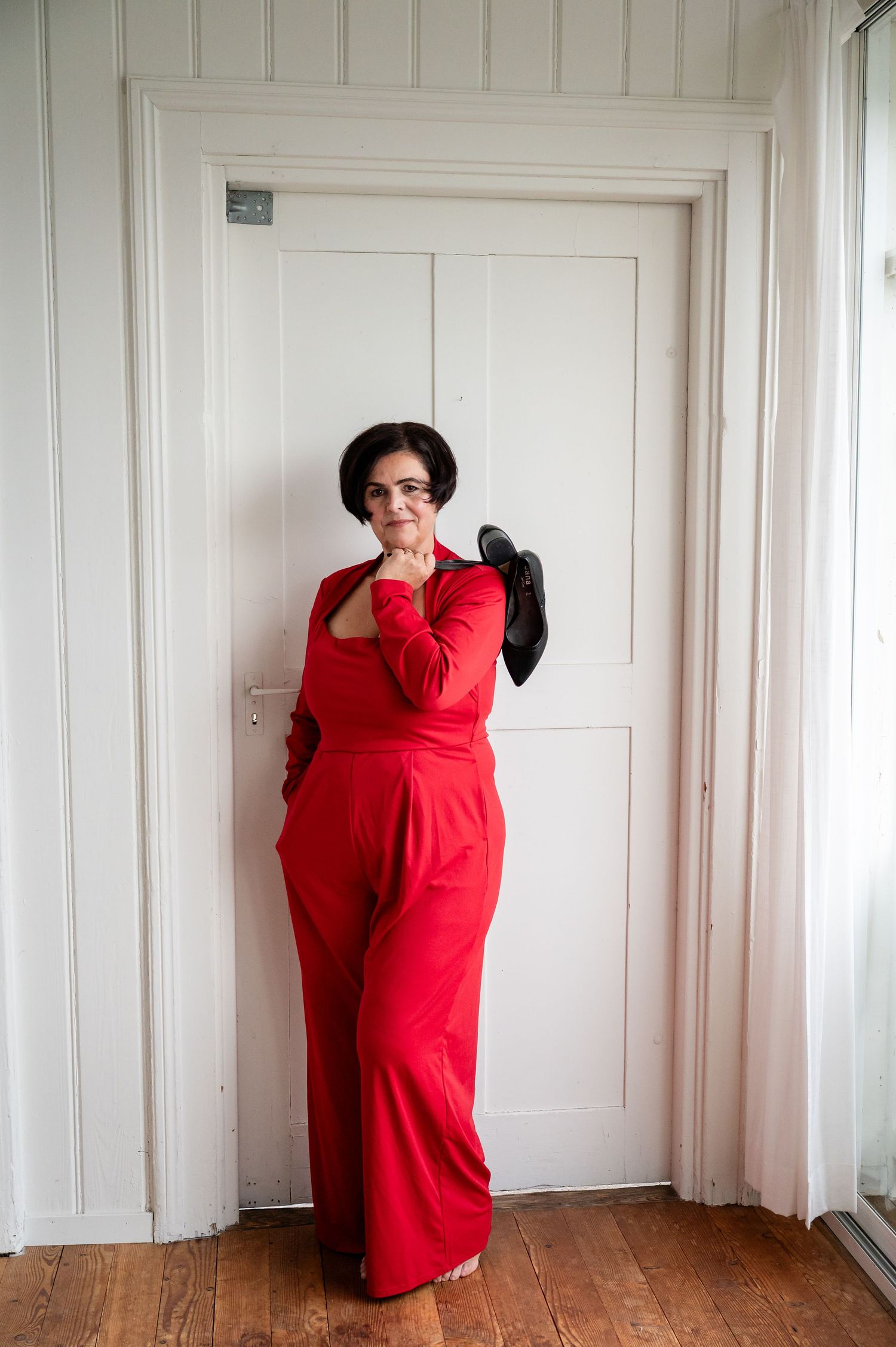 Frau im roten Jumpsuit lehnt selbstbewusst an der Tür – Selbstliebe-Fotoshooting im Raum Thun, Bern.