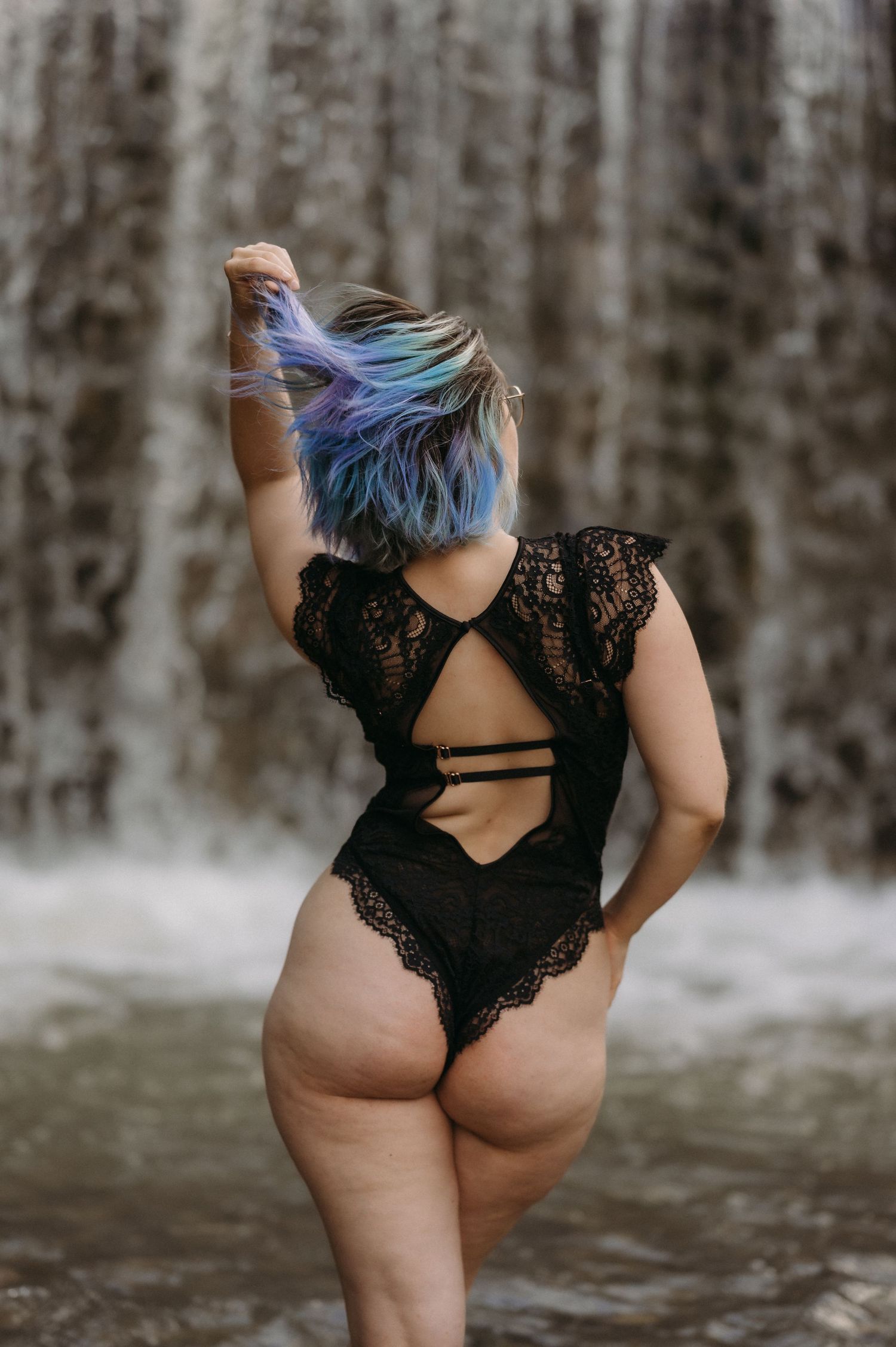 Frau mit bunten Haaren im schwarzen Body vor Wasserfall an der Gürbe – sinnliches Boudoirbild mit Rückenansicht und Naturkulisse.