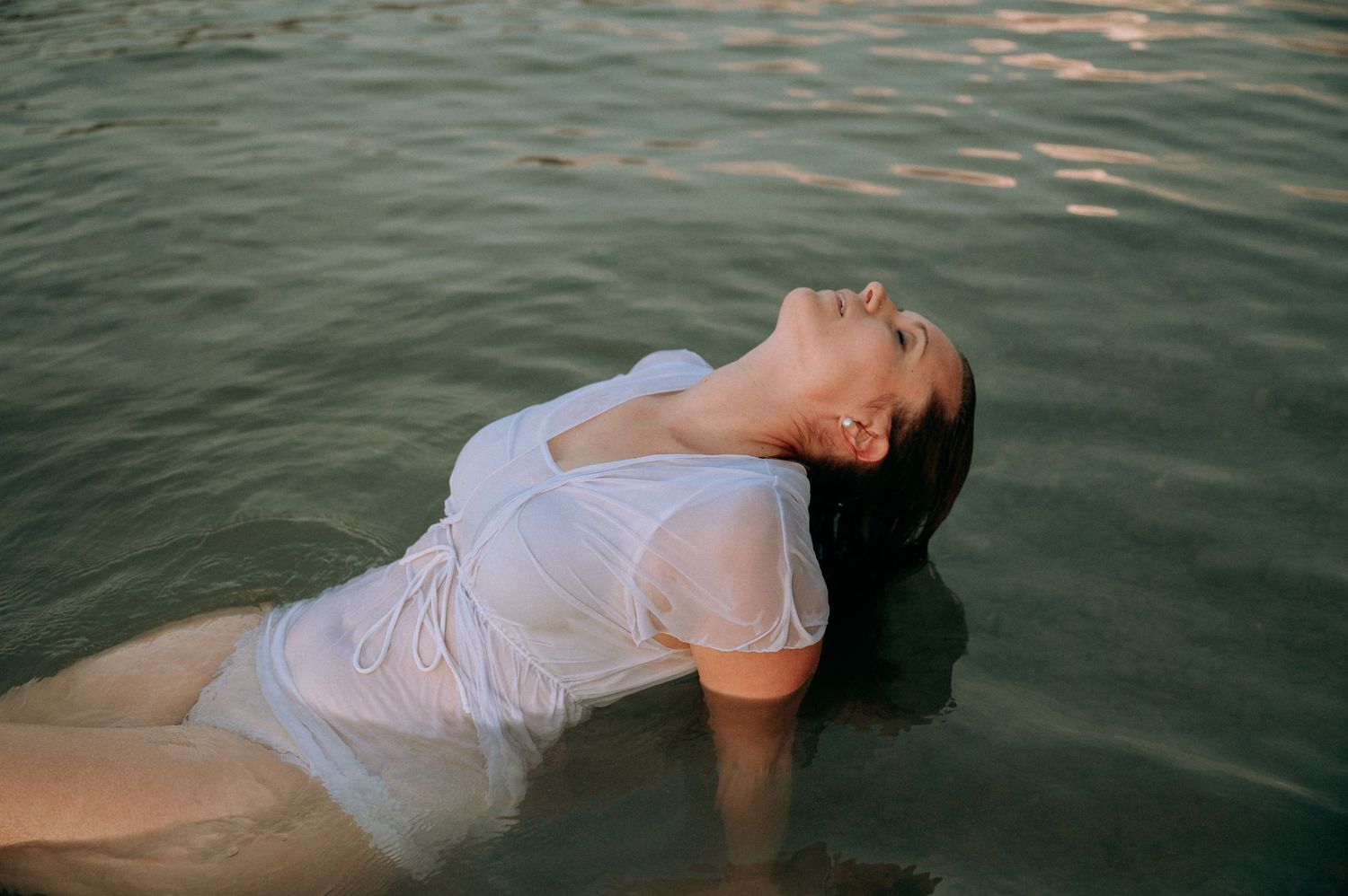 Boudoir-Shooting im Thunersee: Frau lehnt sich entspannt im Wasser zurück, nasses Shirt, geschlossene Augen – sinnlich und frei.