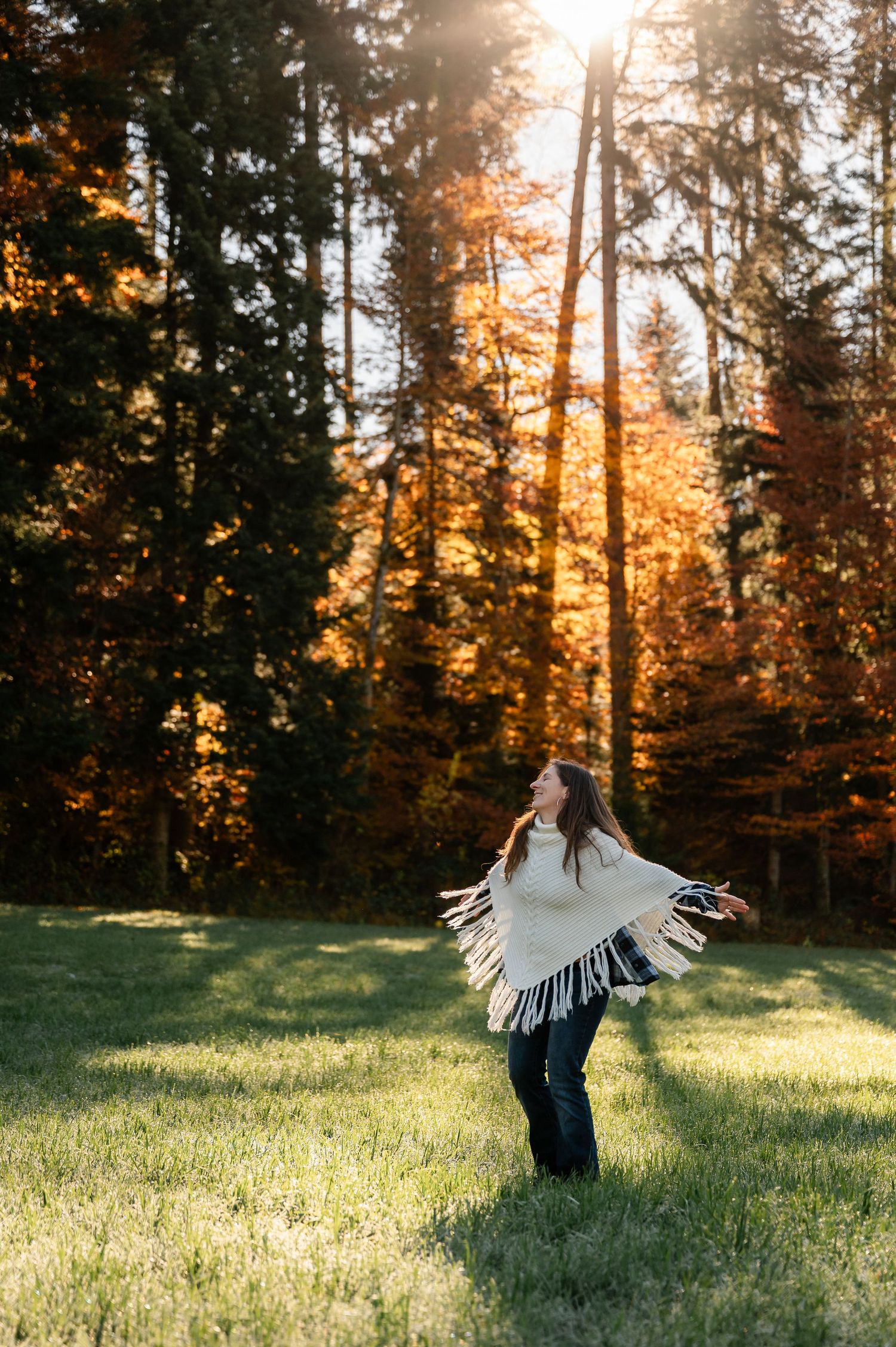 Frau im Poncho tanzt im Morgenlicht vor herbstlich leuchtendem Wald – sinnliches Portrait in der Natur bei Thun im Berner Oberland.
