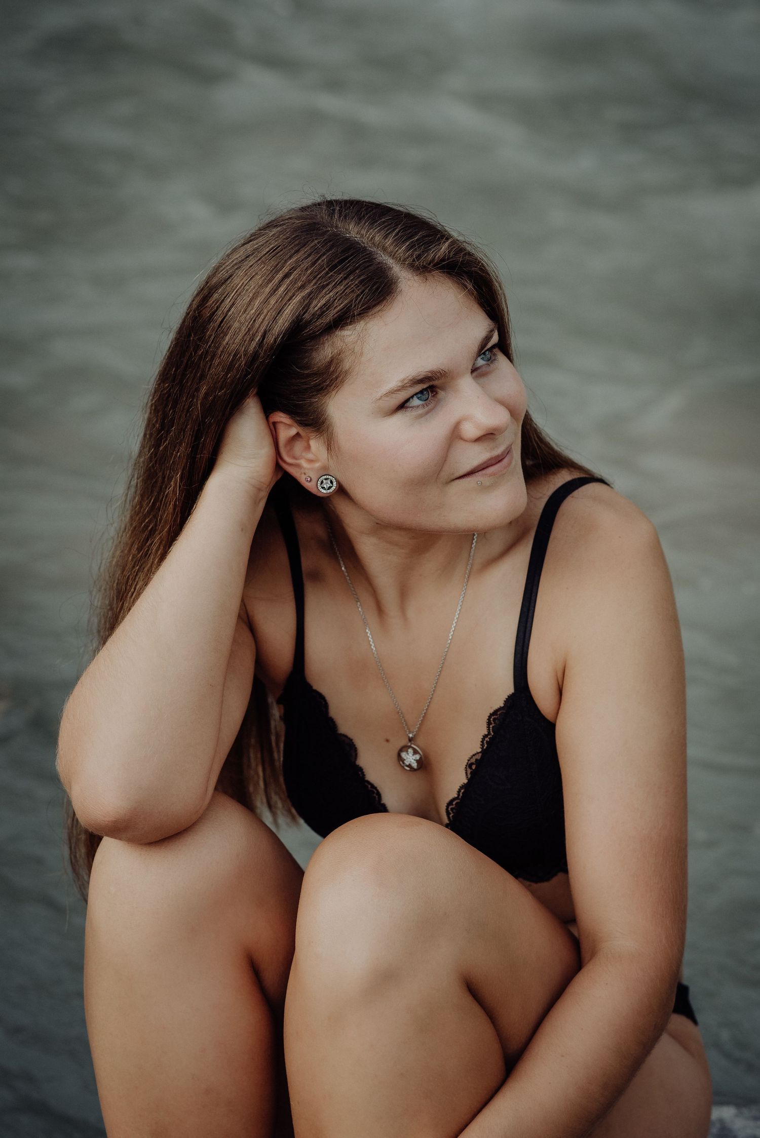 Selbstbewusst und frei: Frau in schwarzer Lingerie sitzt auf einem Felsen an einem Fluss bei Thun, das Haar weht im Wind.