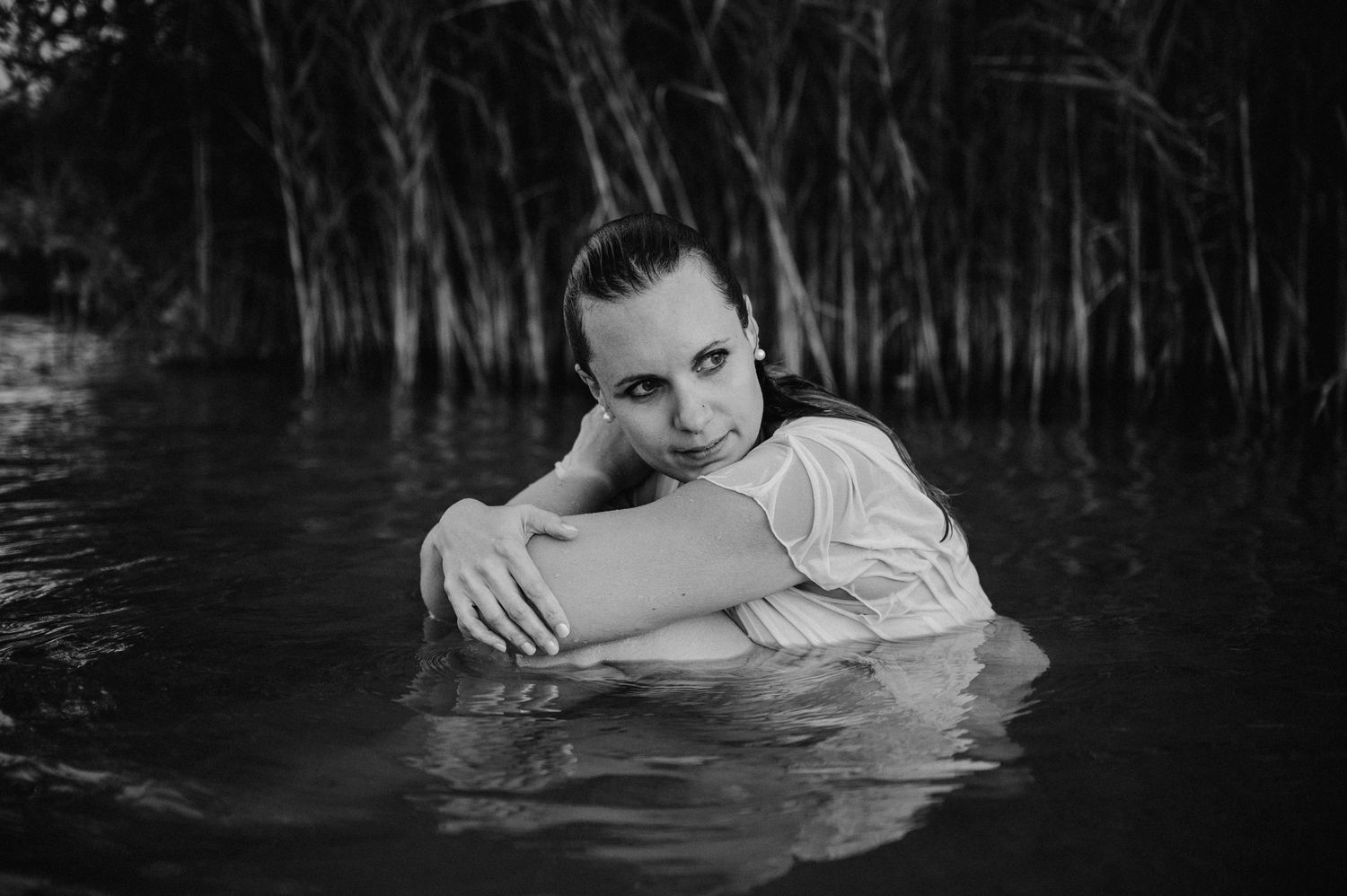 Boudoir-Foto in Schwarz-Weiss: Frau in nassem Kleid umarmt ihre Beine und sitzt still im Wasser – sinnlich, verletzlich, ruhig.