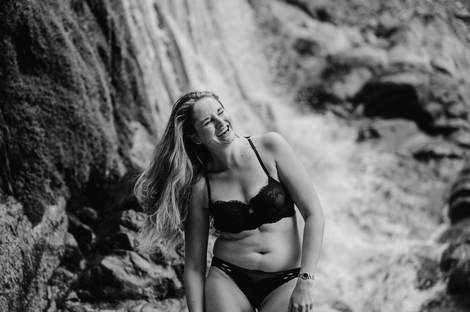 Frau in schwarzer Lingerie posiert selbstbewusst vor Wasserfall bei Thun – sinnliches Boudoirshooting in der Natur.