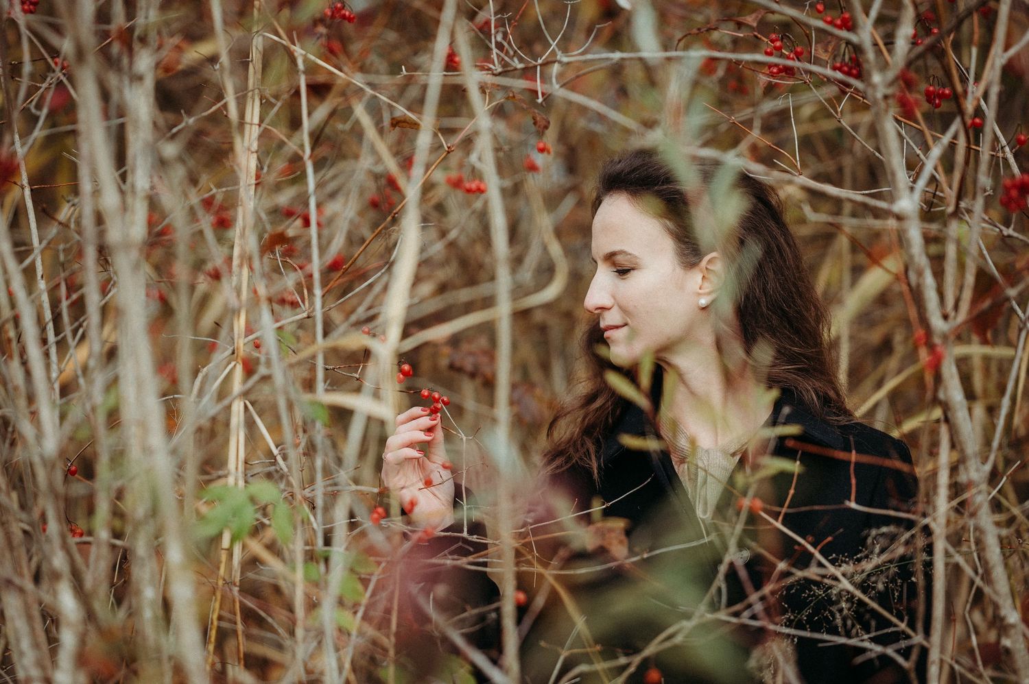 Frau im herbstlichen Gestrüpp mit roten Beeren – stimmungsvolles Herbst-Shooting in der Natur mit sanfter, verträumter Ausstrahlung.