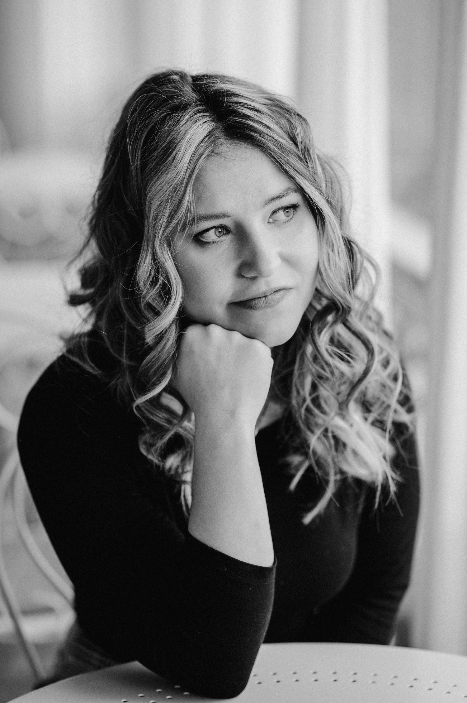 A black and white portrait series showing a person in a dark top with curled hair making contemplative poses.