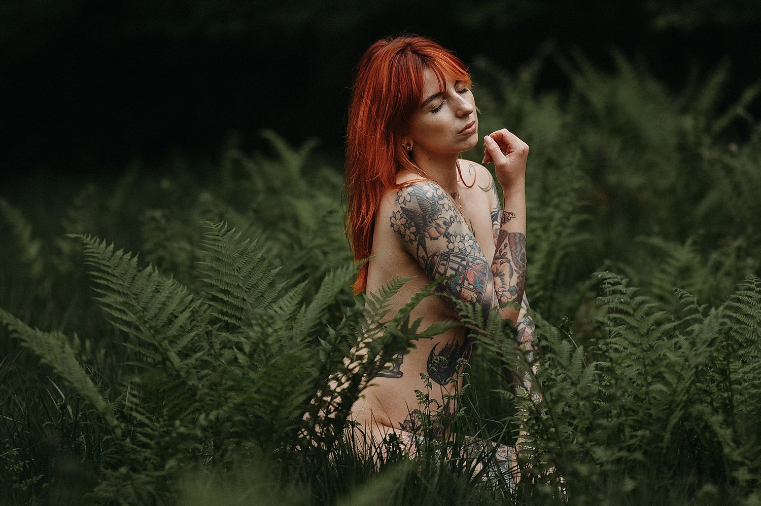 Frau mit rotem Haar und Tattoos sitzt in hohem Farm bei einem Boudoirshooting im Wald