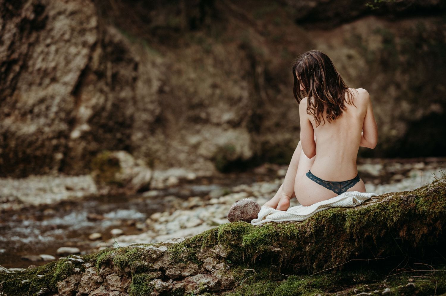 Natürliche Sinnlichkeit: Frau sitzt halbnackt auf einer Decke am Bach. Boudoirshooting in der Nähe von Thun, Schweiz.