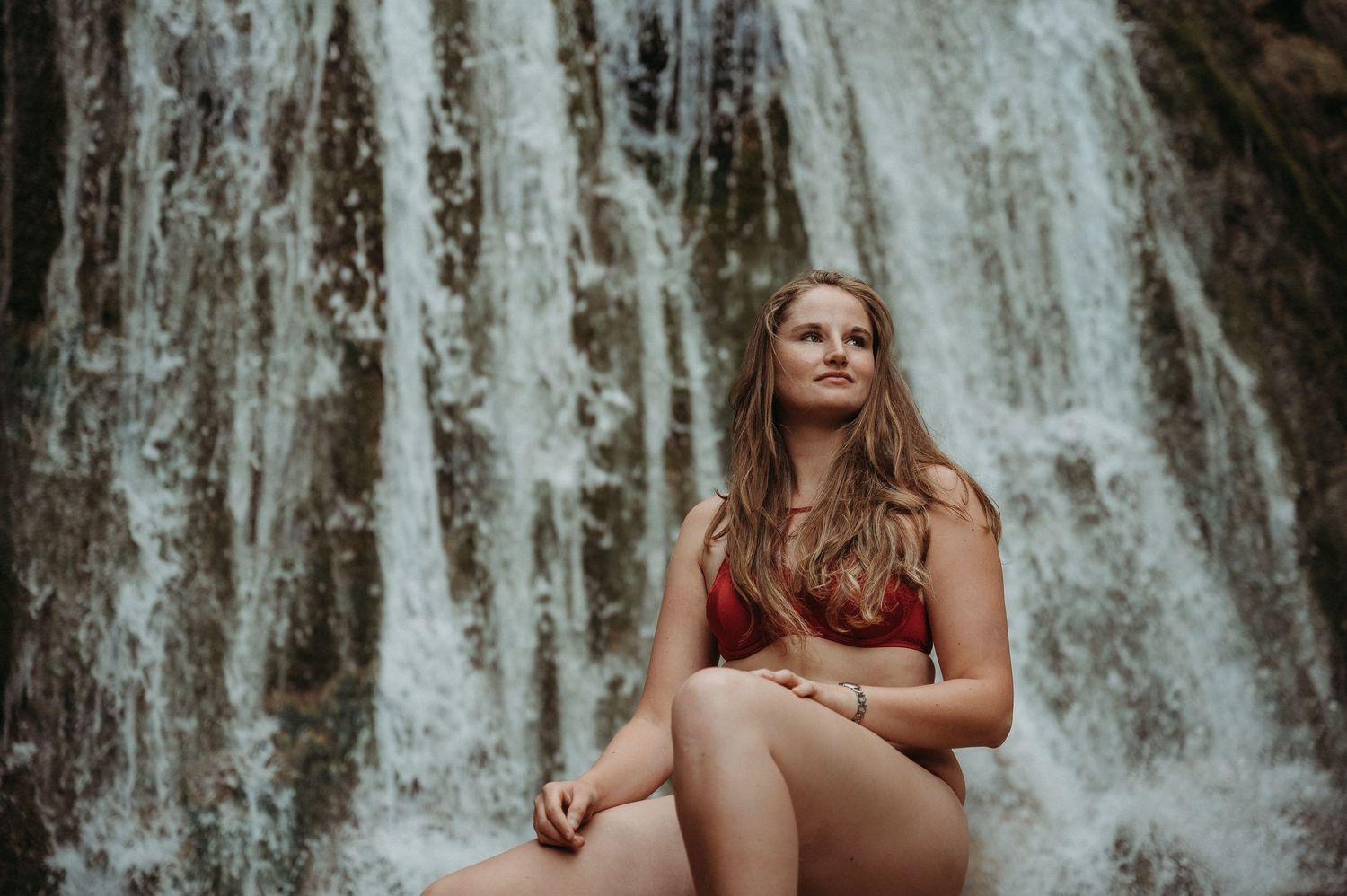 Selbstbewusste Frau in roter Lingerie sitzt vor Wasserfall bei Thun – Boudoirbild voller Sinnlichkeit, Stärke und natürlicher Schönheit.