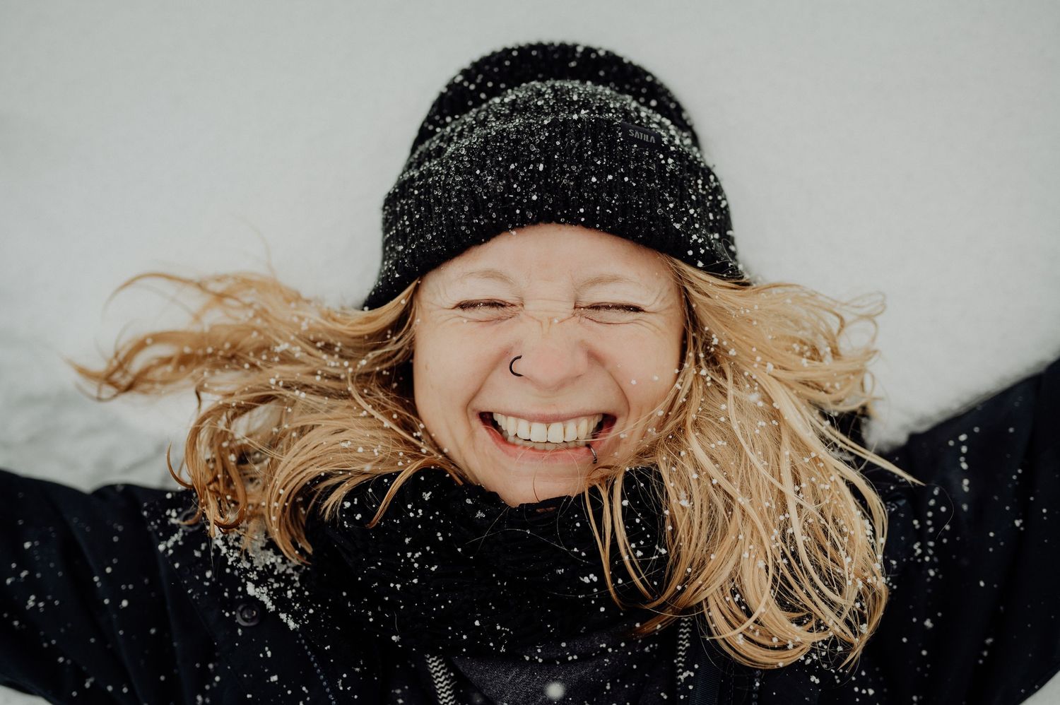 Frau mit Mütze liegt im SchneeBerner Oberland. Portraitshooting in der Natur mit Spass und Winterzauber.