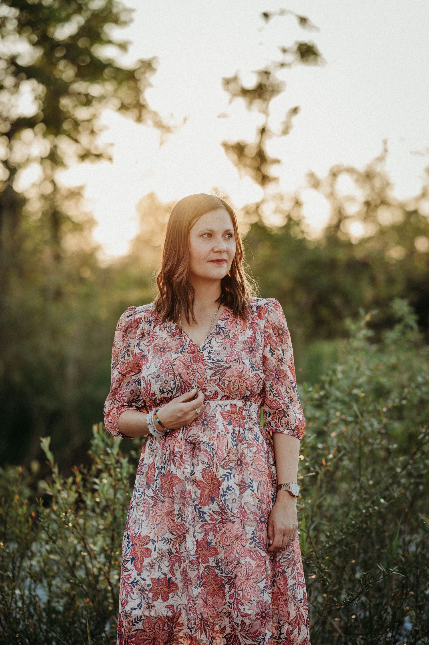 Frau mit mittellangem Haar im gemusterten Kleid steht in der Natur bei Sonnenuntergang – Outdoor-Portrait