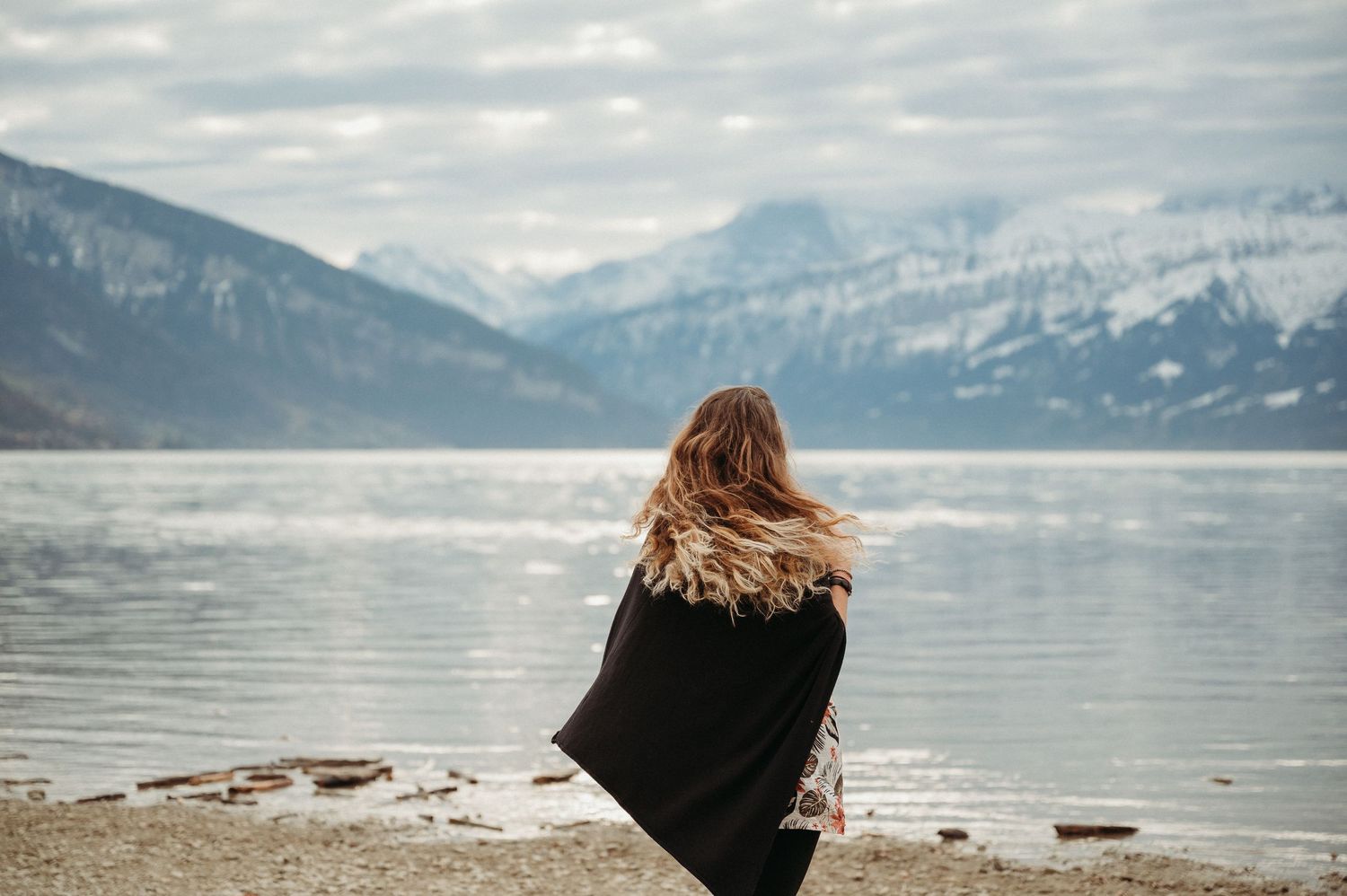 Frau im schwarzen Cape steht am winterlichen See – natürliches Porträt am winterlichen Thunersee