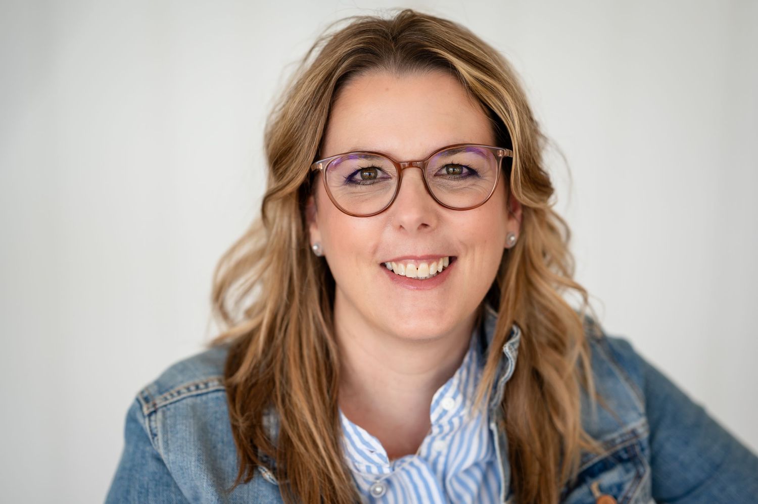 Portrait einer lächelnden Frau mit Brille und Jeansjacke – authentisch und kompetent im Business-Coaching unterwegs.