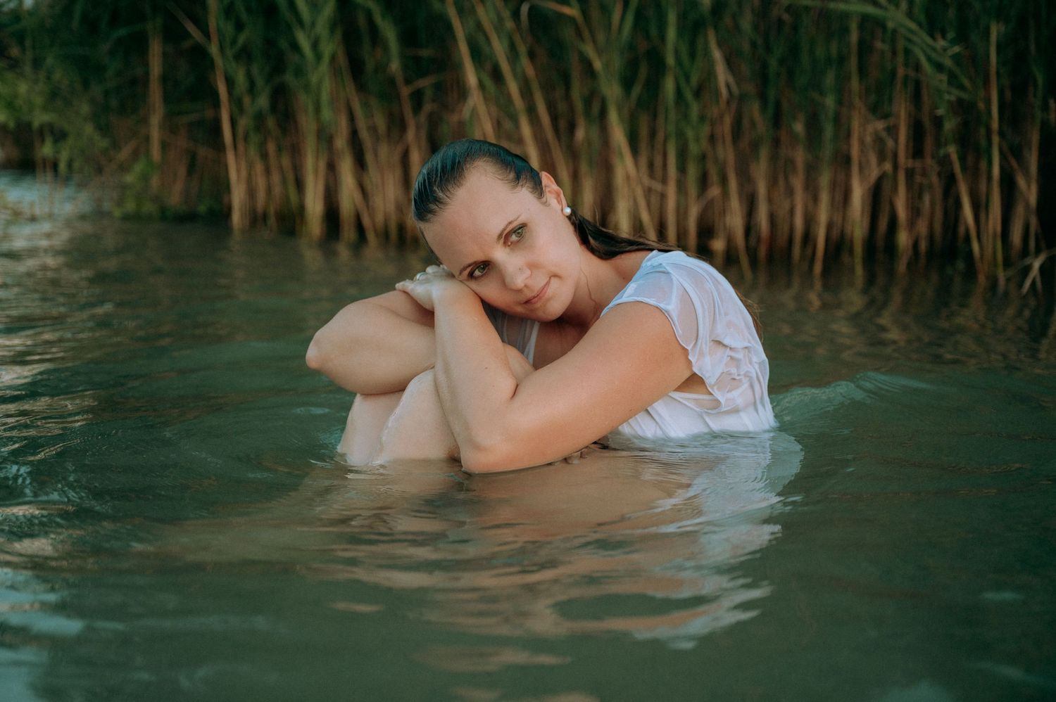 Frau sitzt in weissem Kleid im Thunersee, umgeben von Schilf – sinnliches Portrait in der Abendstimmung.