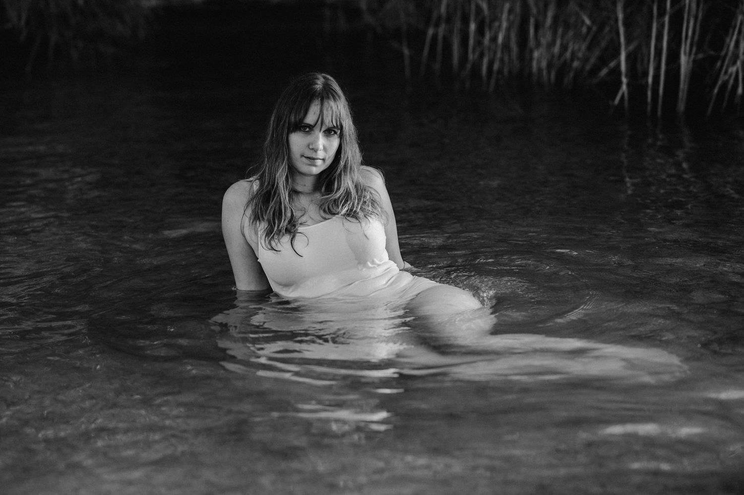 Boudoir-Shooting im Thunersee: Frau treibt in nassem Kleid im Wasser, Blick zur Kamera – sinnlich, ruhig, verwoben mit der Natur.