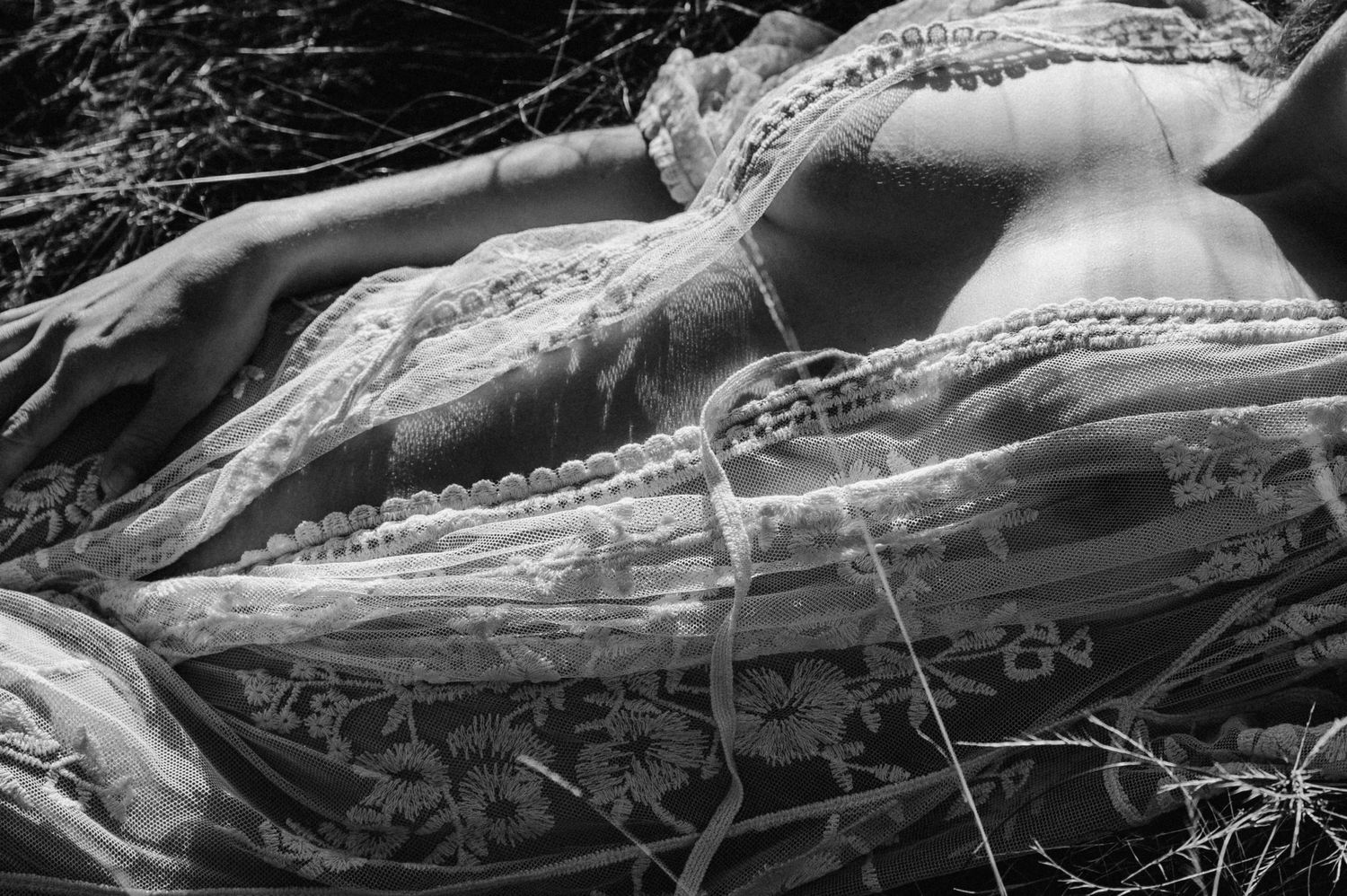 Detailaufnahme eines Boudoir-Shootings: Eine Frau liegt in transparenter Spitzenrobe im Gras, Licht und Schatten betonen sanft die Formen.