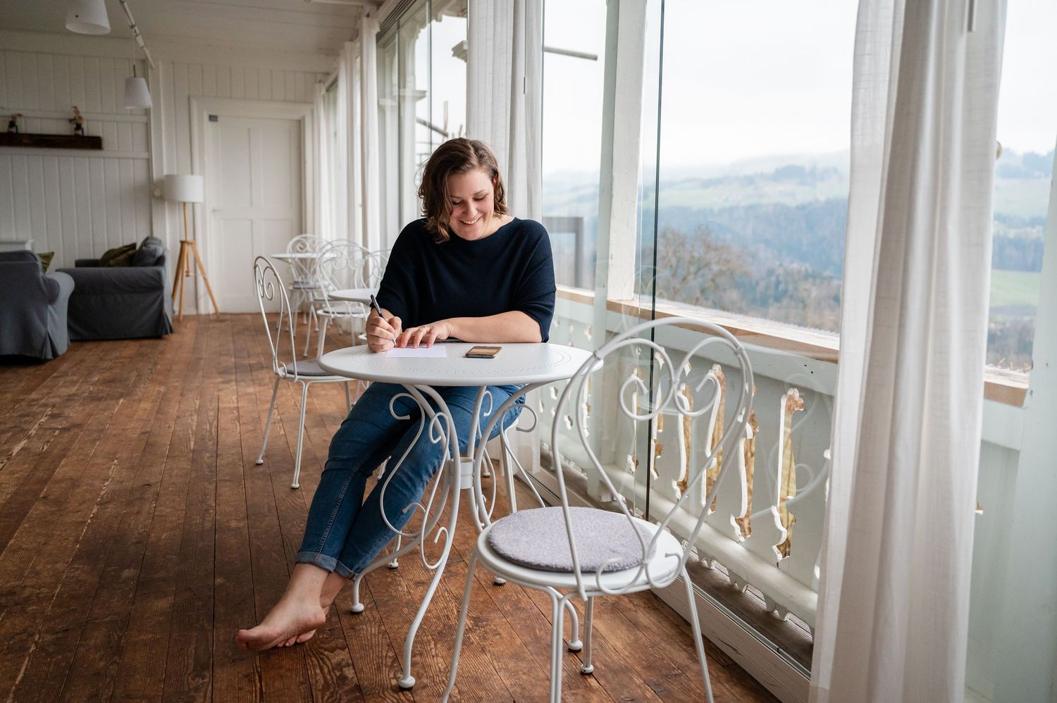 Authentisches Portrait einer Familiencoachin beim Schreiben – lichtdurchfluteter Raum mit Ausblick und ruhiger Atmosphäre