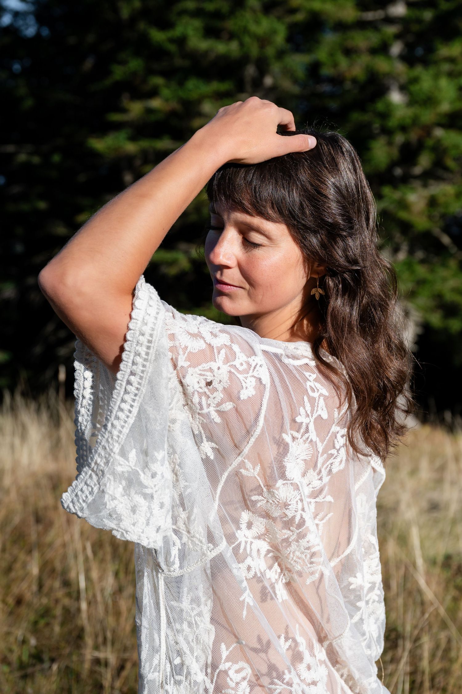 Sinnliches Boudoir-Porträt einer Frau im Spitzenkleid auf einer Wiese, im Sonnenlicht mit geschlossenen Augen und entspannter Pose.