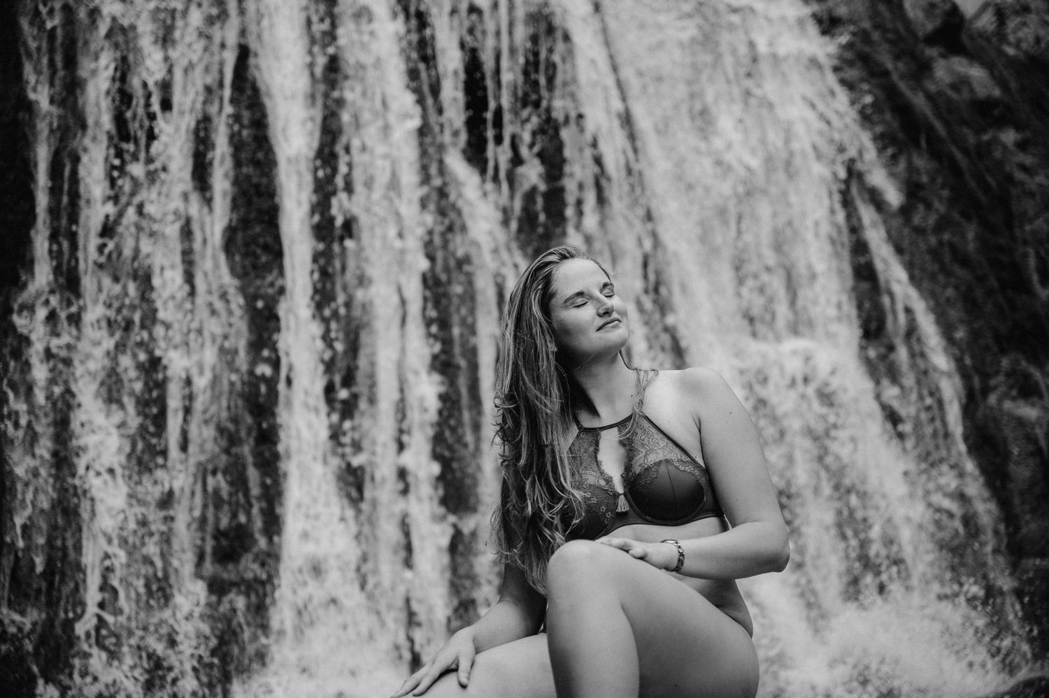 Frau in schwarzer Lingerie posiert selbstbewusst vor Wasserfall bei Thun – sinnliches Boudoirshooting in der Natur.