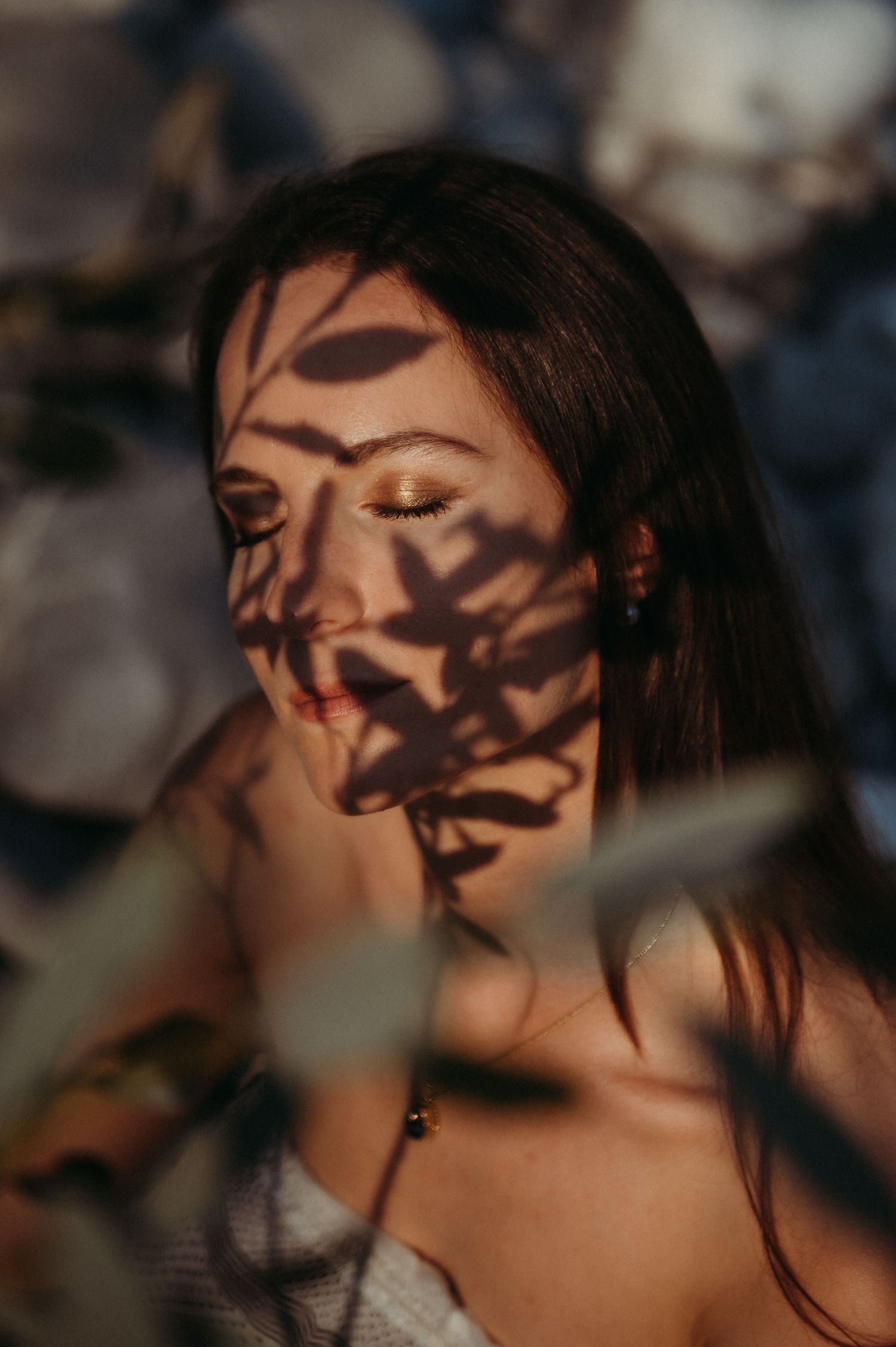 Frau mit geschlossenen Augen, von Blätterschatten gemustert – stimmungsvolles Portrait mit Licht und Natur im Fokus.