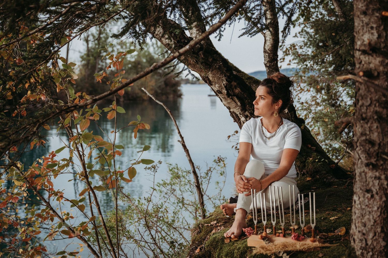 Frau in heller Kleidung sitzt mit kinesiologischen Essenzen im Wald am Seeufer – Businessfoto für ganzheitliche Heilpraxis