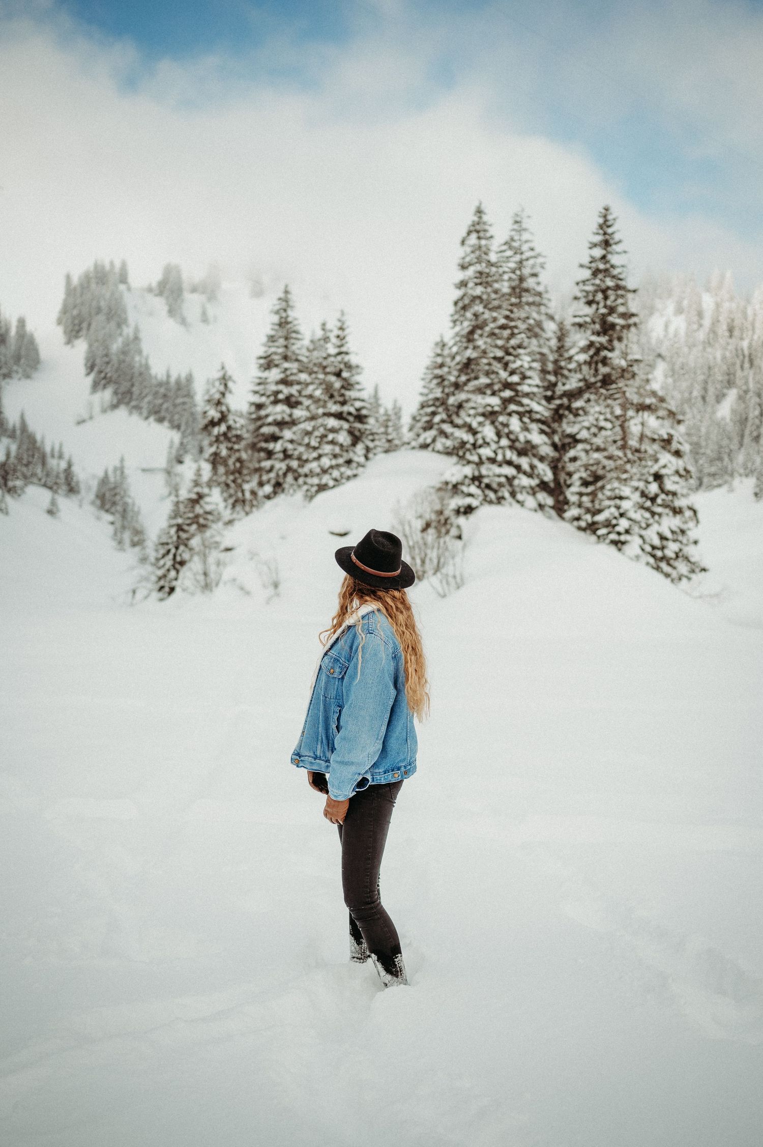Frau mit Hut im tief verschneiten Winterwald im Berner Oberland. Portraitshooting in der Natur mit Weitblick und Winterzauber.