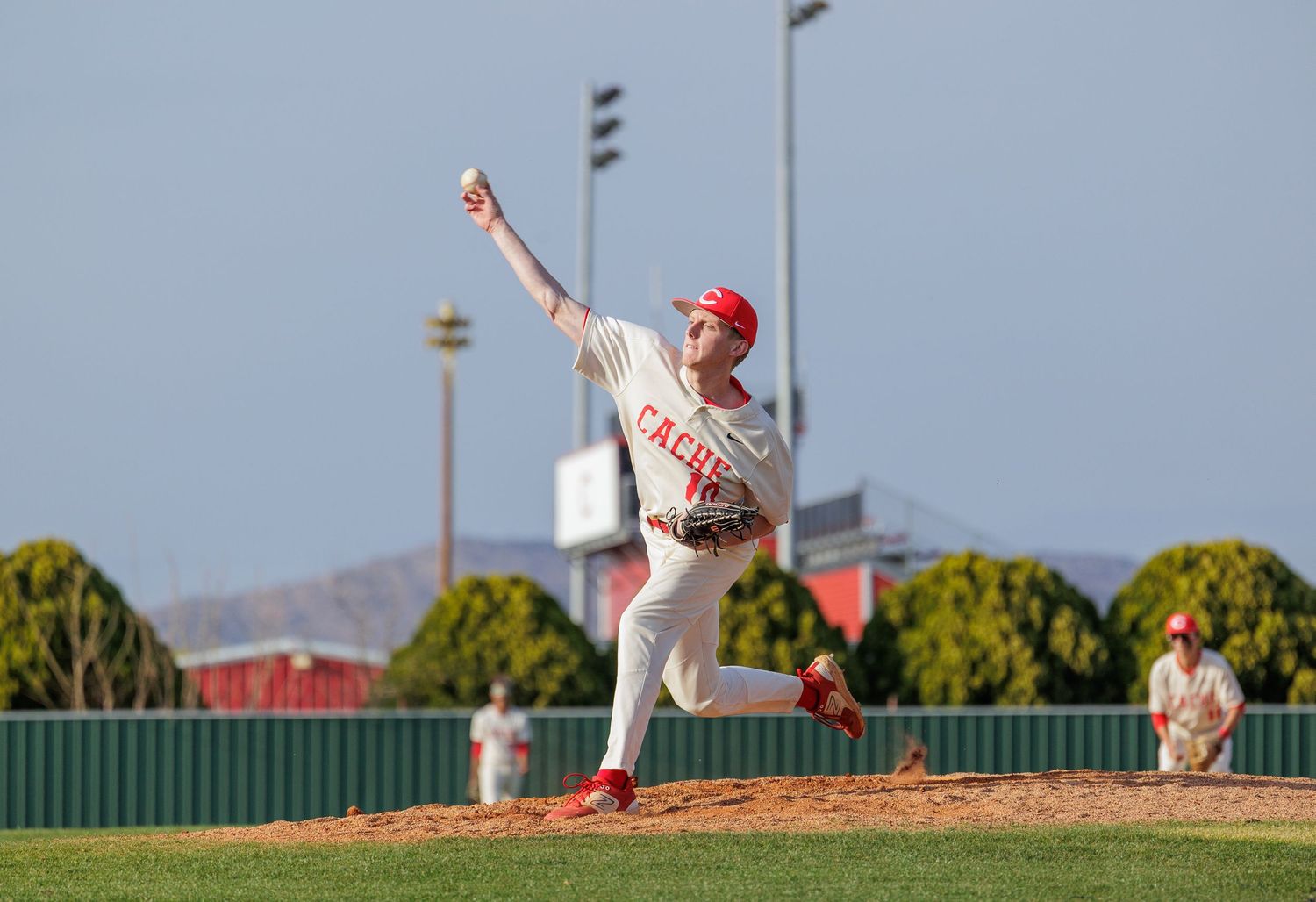 Baseball pitcher in white and red uniform winds up to throw during a game on a sunny day.