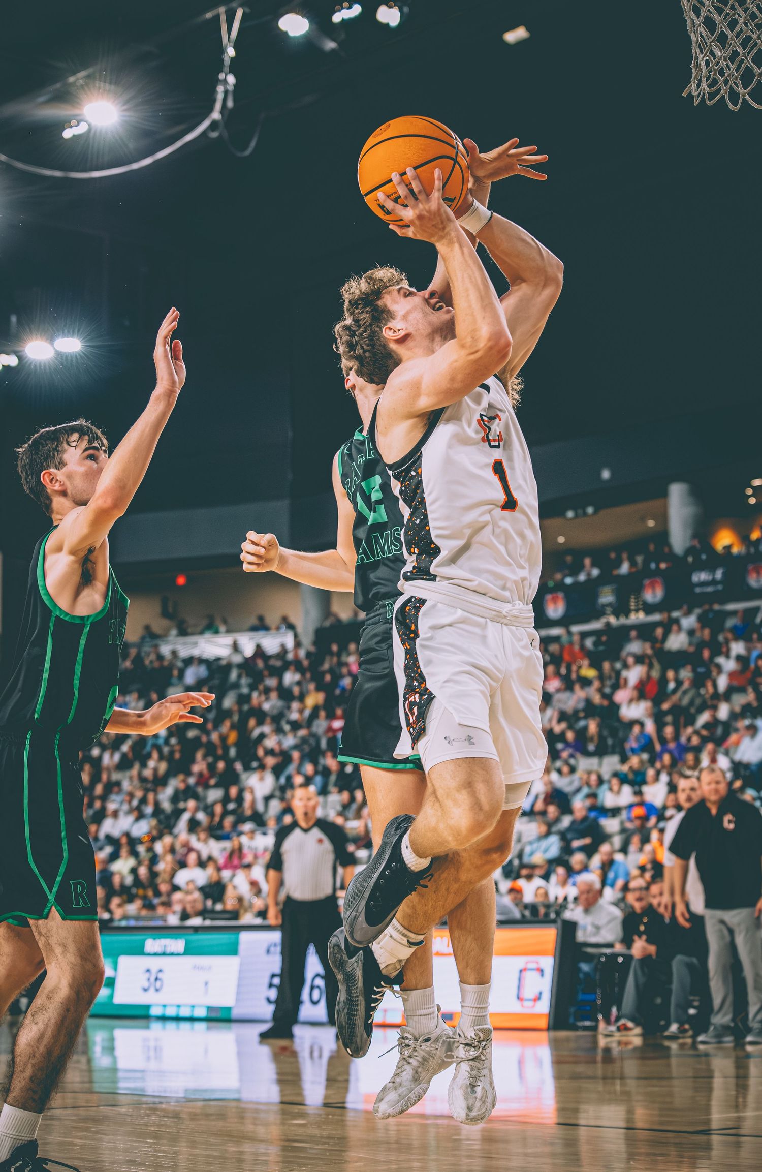 Basketball player #1 drives to the basket against a defender in a packed arena game.