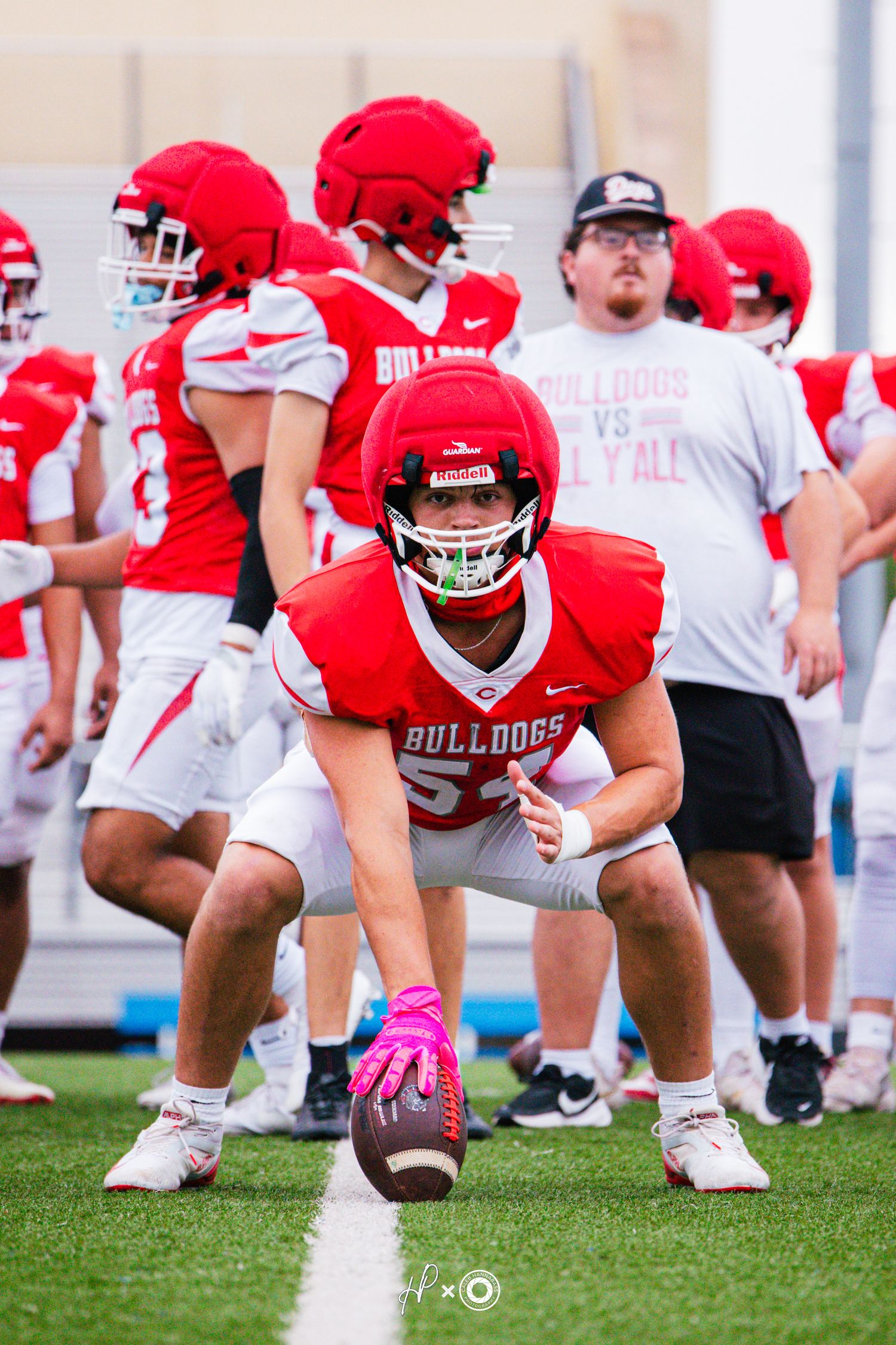 A Bulldogs football player in red uniform crouches over the ball at the line of scrimmage during a practice session.