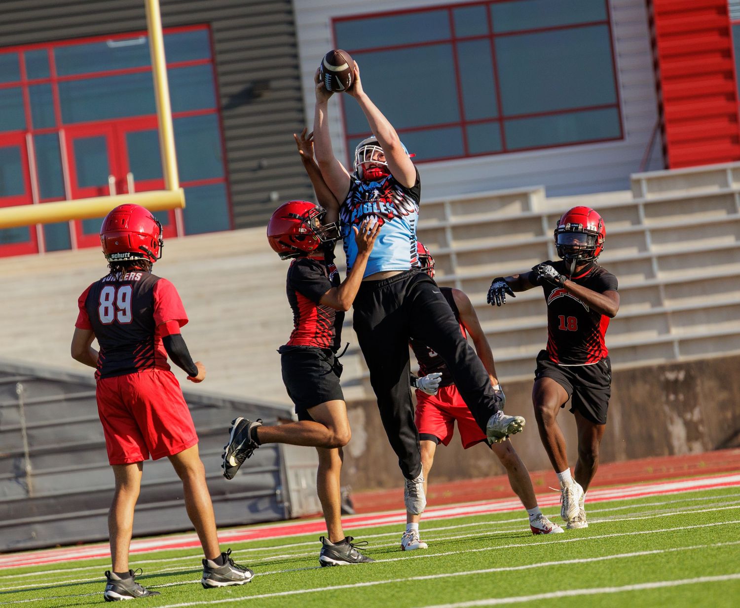 Football player leaps to catch a ball over defenders during a competitive practice drill at a stadium.