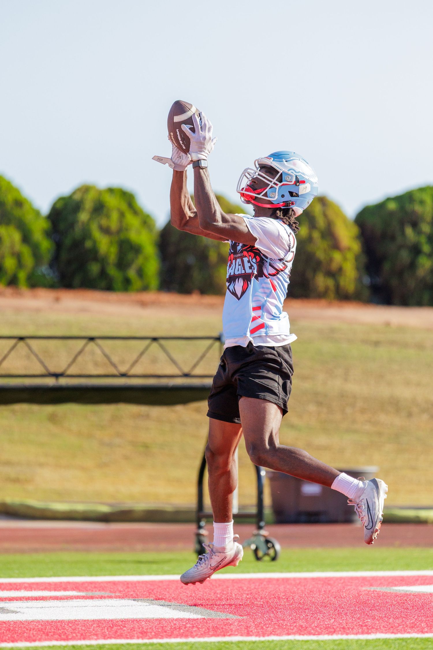 Football player in white uniform leaps to catch a pass in the end zone during practice.