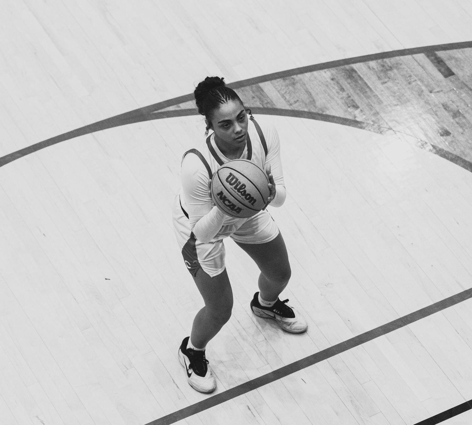 Overhead black and white photo of female basketball player holding Wilson ball on court.