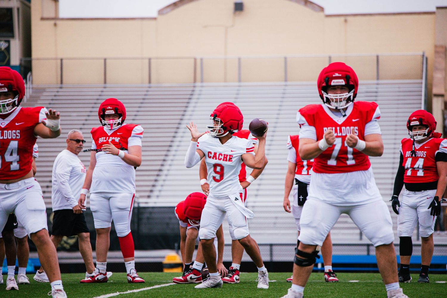 High school football players in red Bulldogs uniforms warm up on the field during practice.