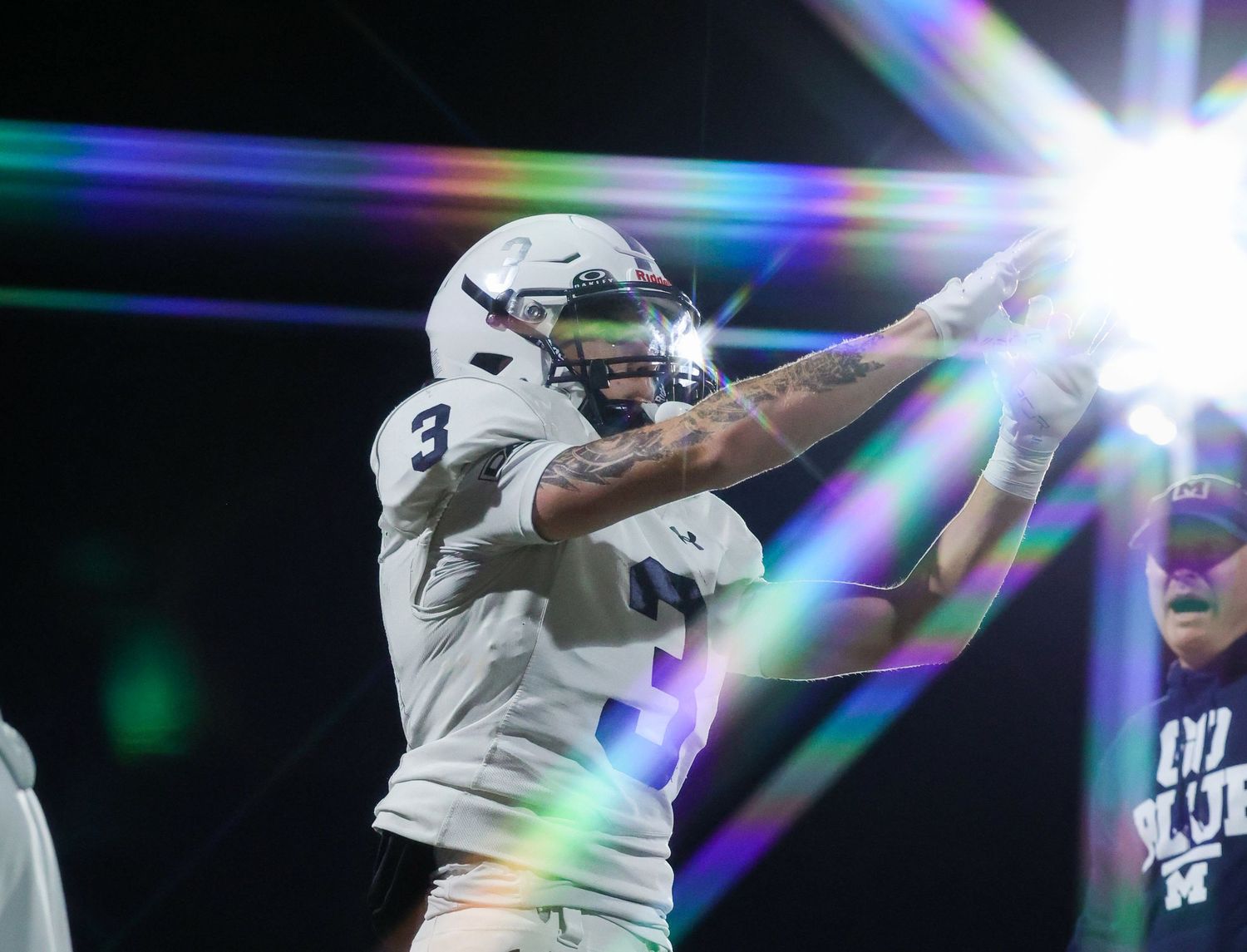 Football player #3 in white uniform celebrates with a teammate under bright stadium lights.