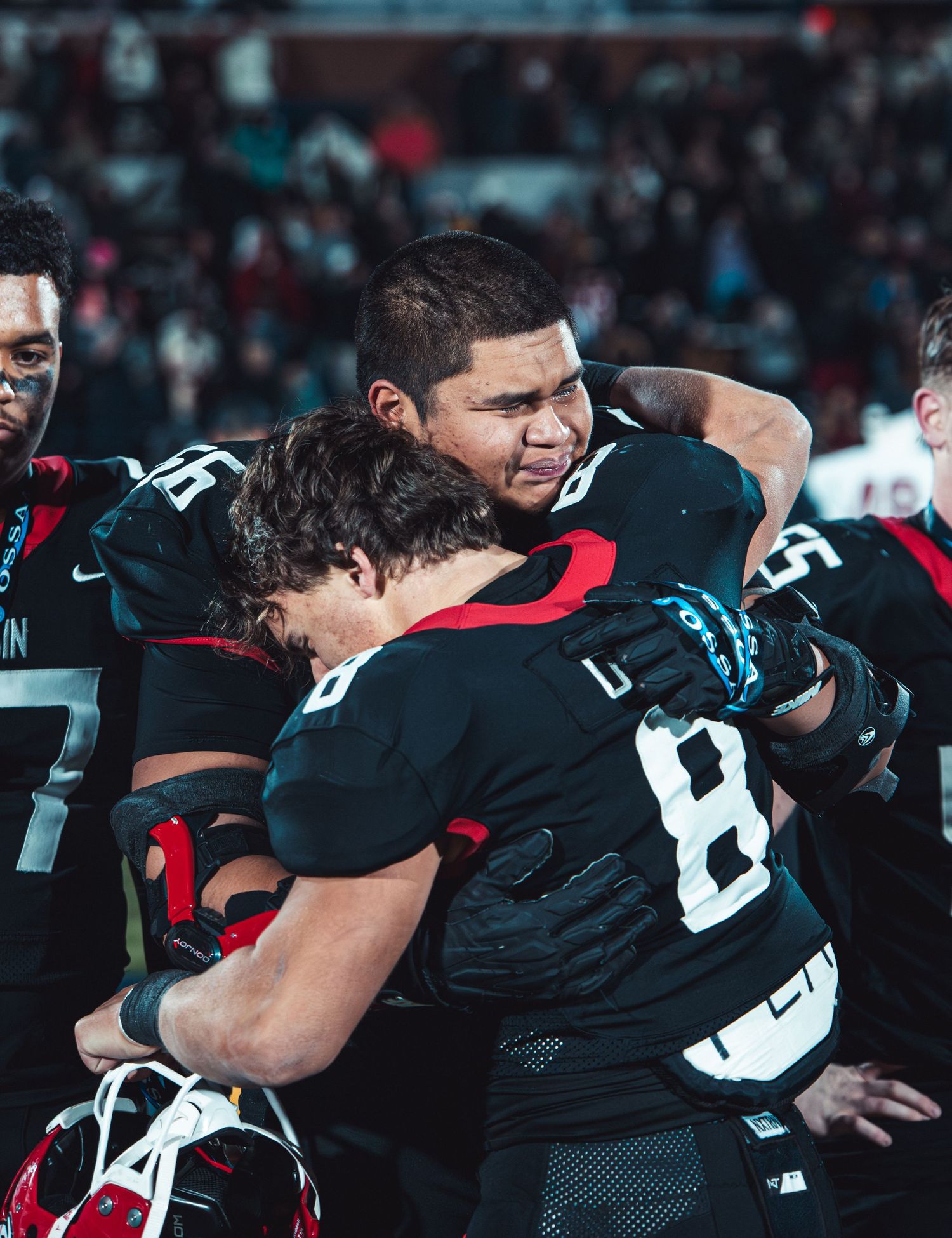 Football players in black uniforms embrace in an emotional moment on the field.