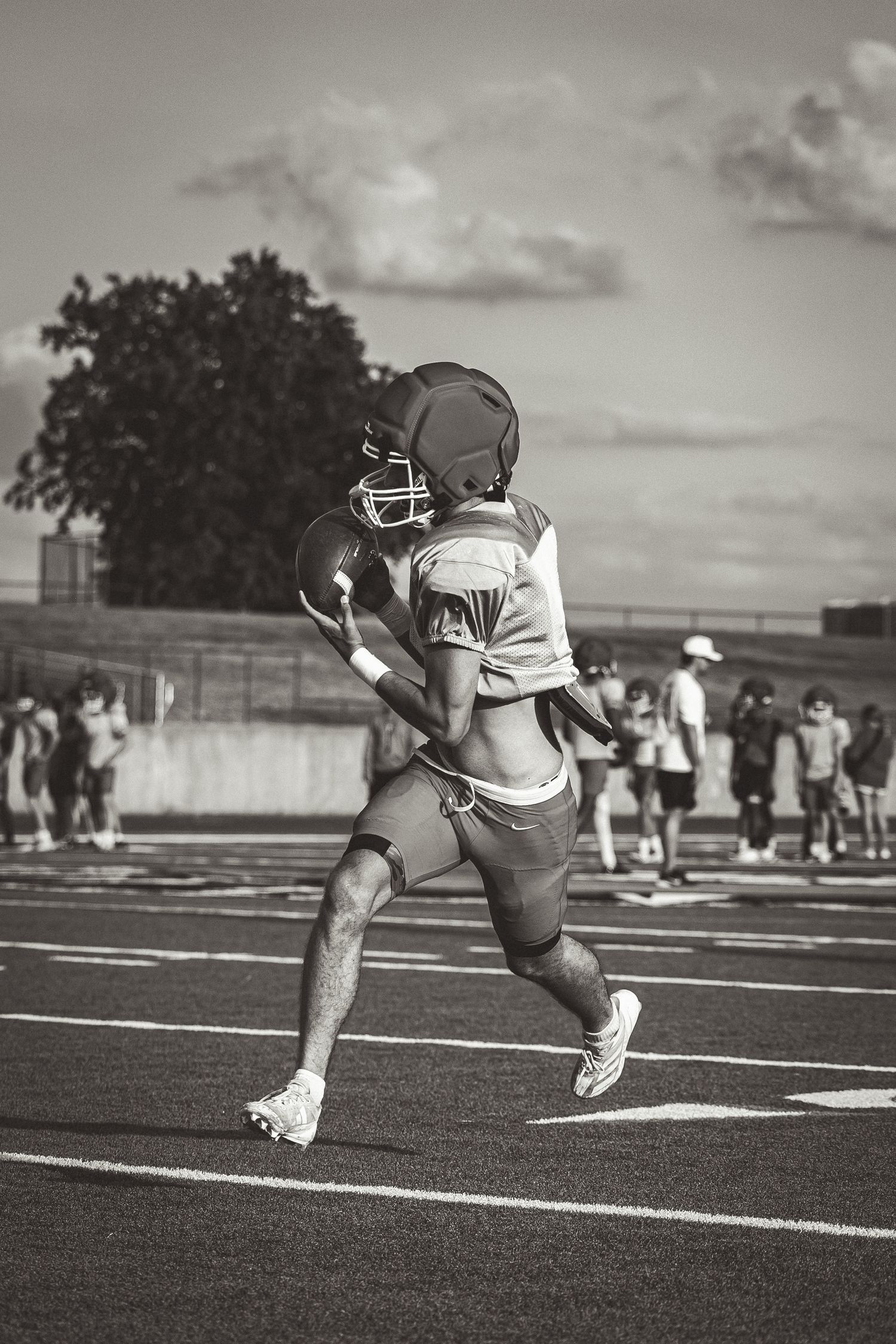 Black and white image of two football players running on a track field during practice.
