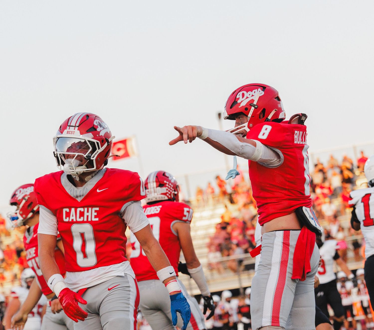 Cache Bulldogs football players in red uniforms celebrate on the field during a high school football game.