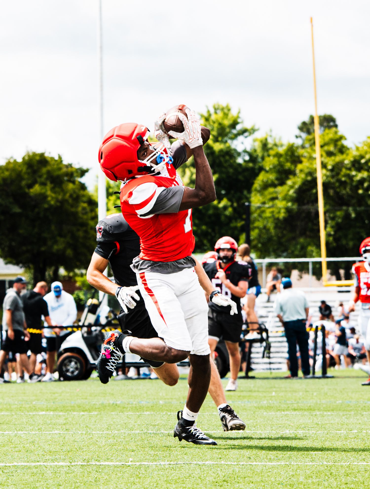 Football player in red uniform leaping to catch a pass during an outdoor practice game.