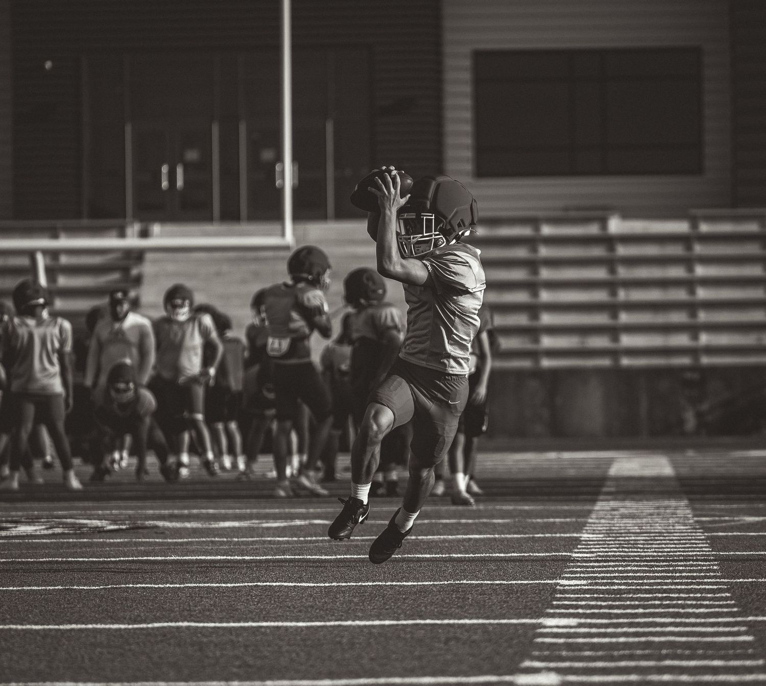 Black and white action shot of a football player leaping to catch a pass during a night game.