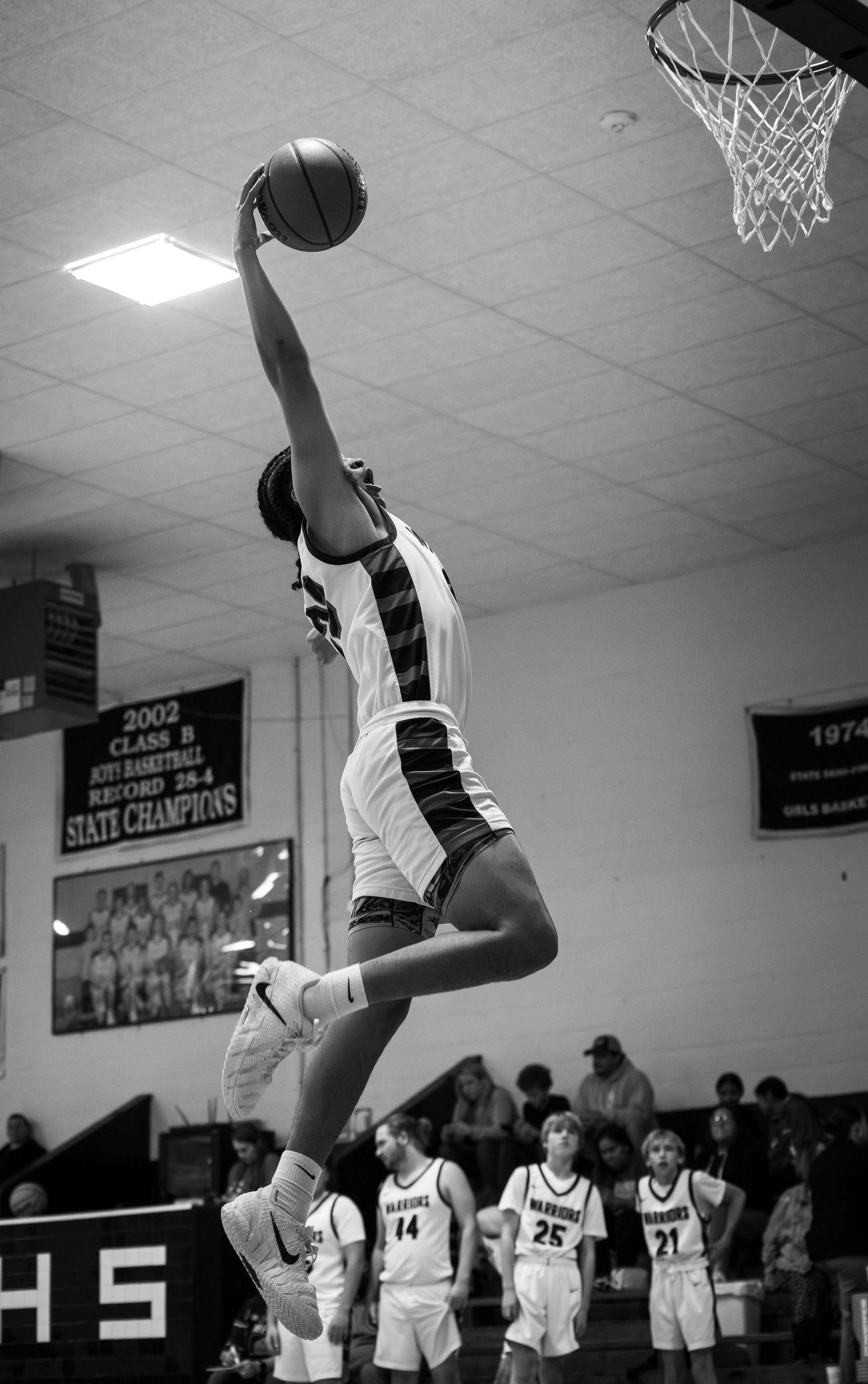 Black and white photo of a basketball player dunking during a high school game.