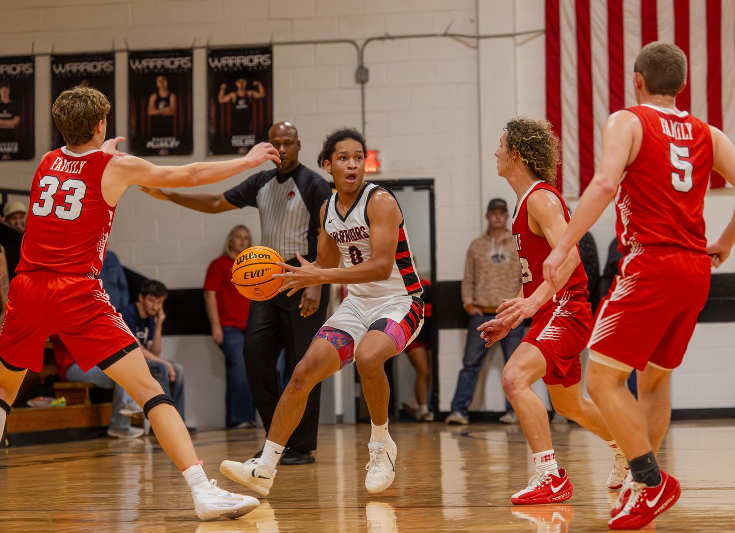 High school basketball player drives to the basket surrounded by defenders in red jerseys during an indoor game.